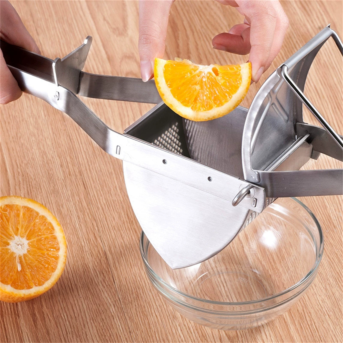 Hände, die eine Orangenscheibe in einer Saftpresse über einer Glasschüssel auf einem Holztisch auspressen.