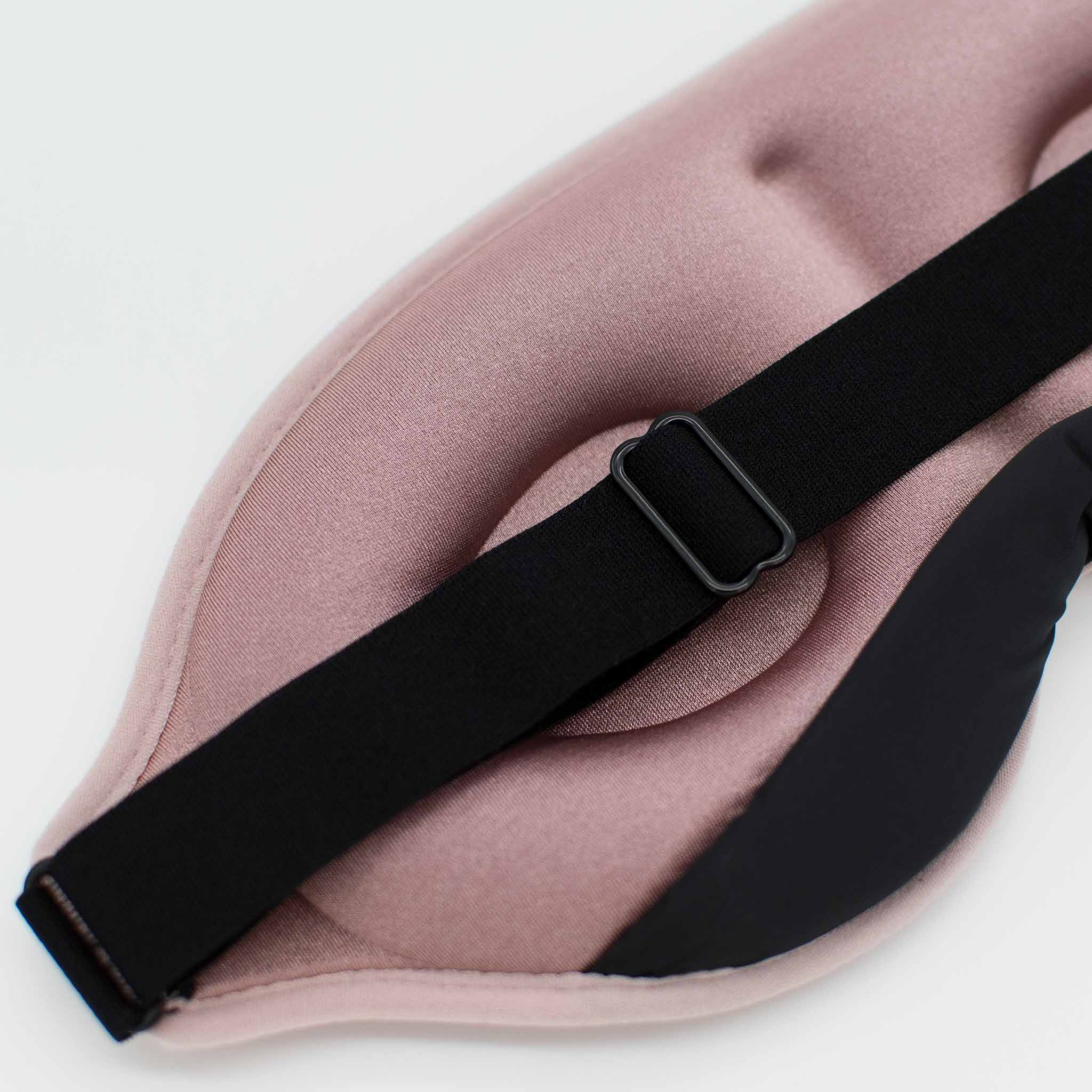 Eine rosa Schlafmaske mit schwarzem Riemen, liegt auf einer weißen Oberfläche.
