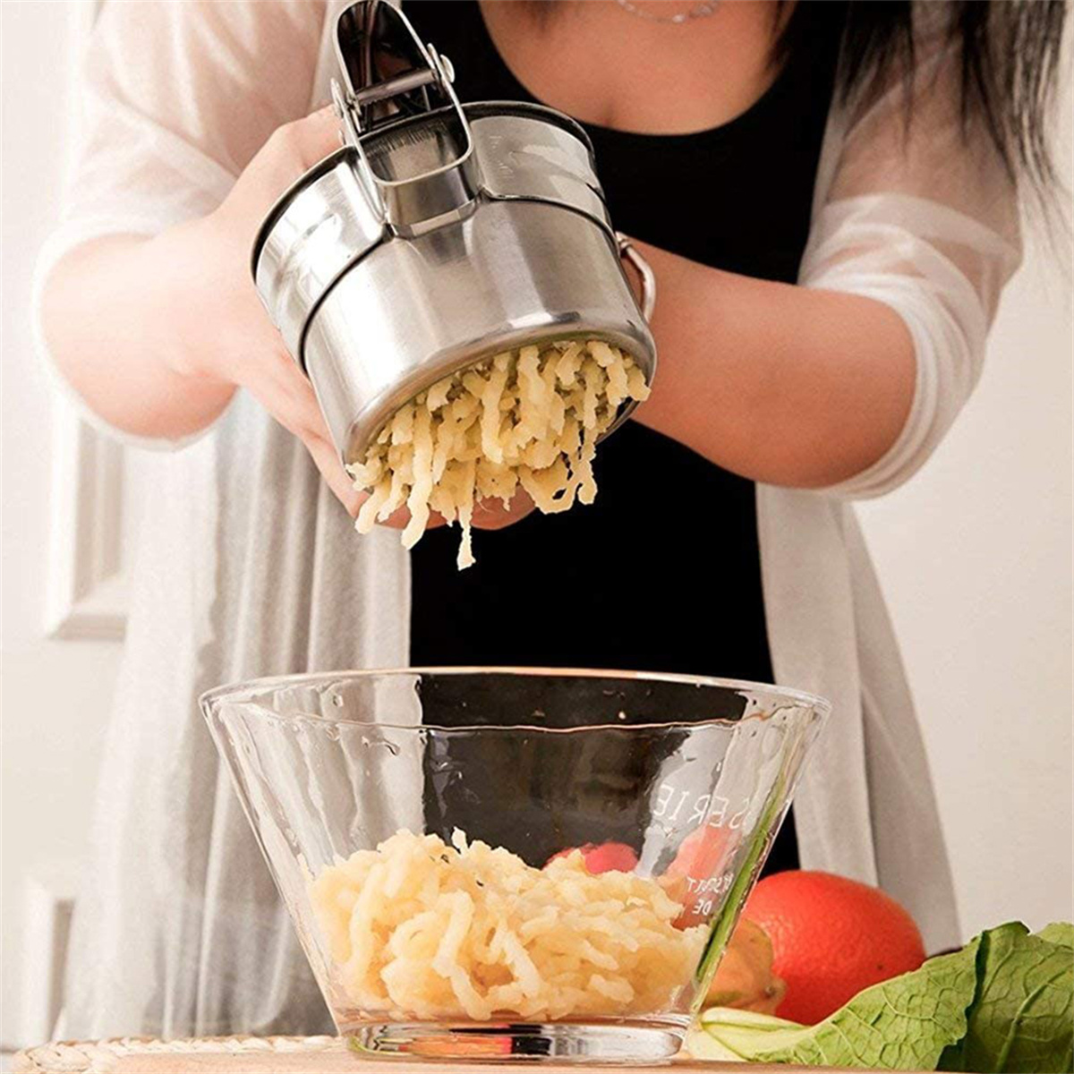 Person drückt Kartoffeln durch eine Kartoffelpresse in eine Glasschüssel.
