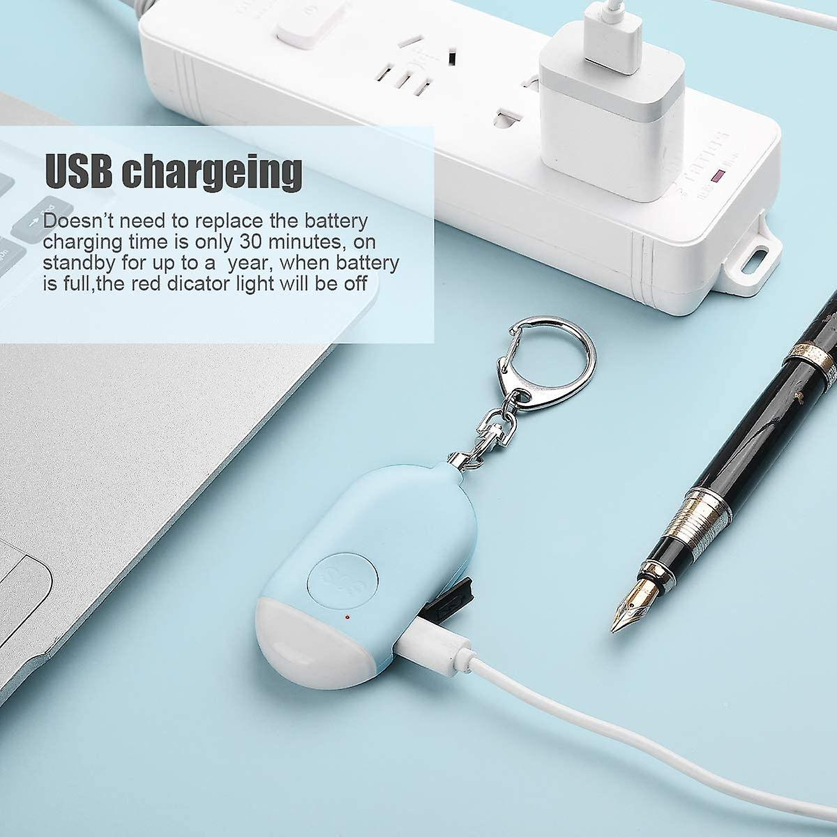 Ein hellblaues persönliches Sicherheitsgerät, das über USB aufgeladen wird. Ein Stift und ein Laptop liegen auf blauem Untergrund.