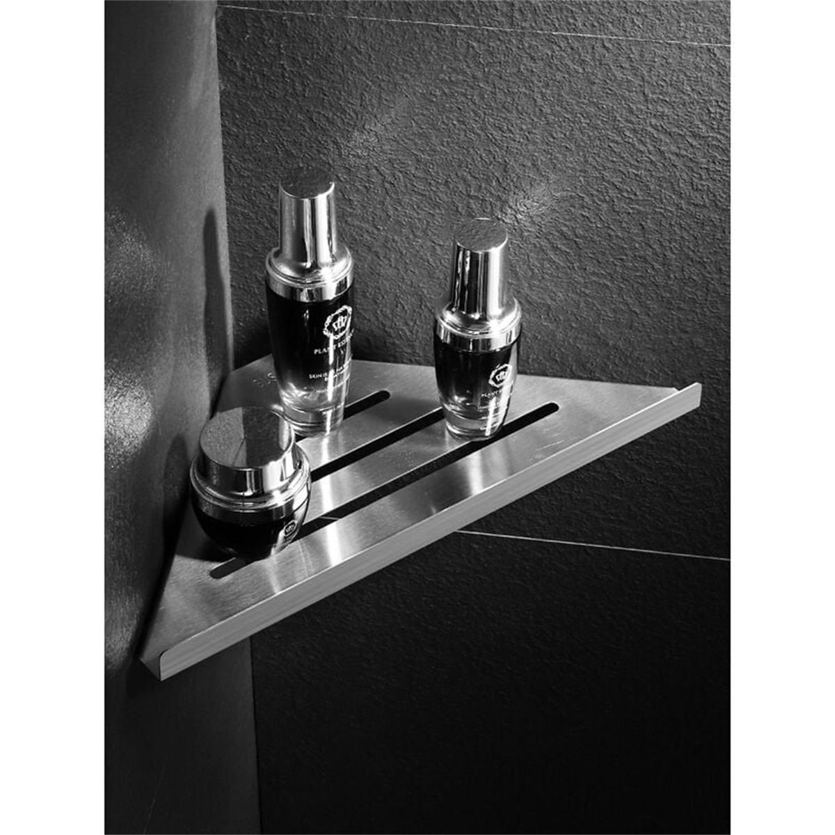 Drei Flaschen Hautpflegeprodukte auf einem Eckregal aus Edelstahl, vor dunkler Wand.