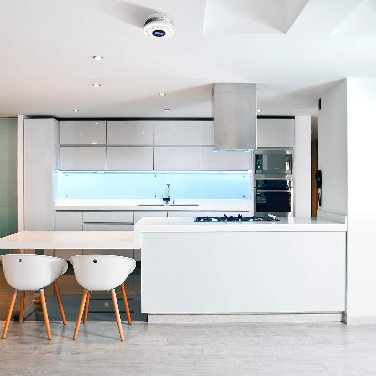 Moderne weiße Küche mit Rauchmelder an der Decke. Weiße Möbel und heller Holzboden.