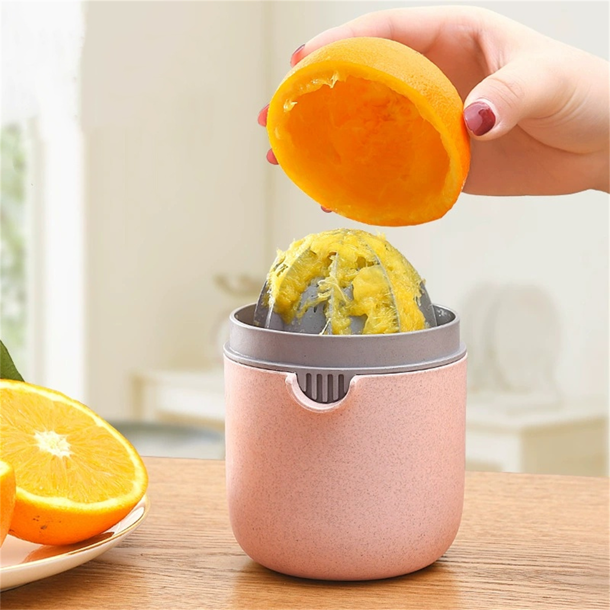 Eine Hand presst eine Orangenhälfte in einen Entsafter; eine halbe Orange auf einem Teller ist sichtbar.