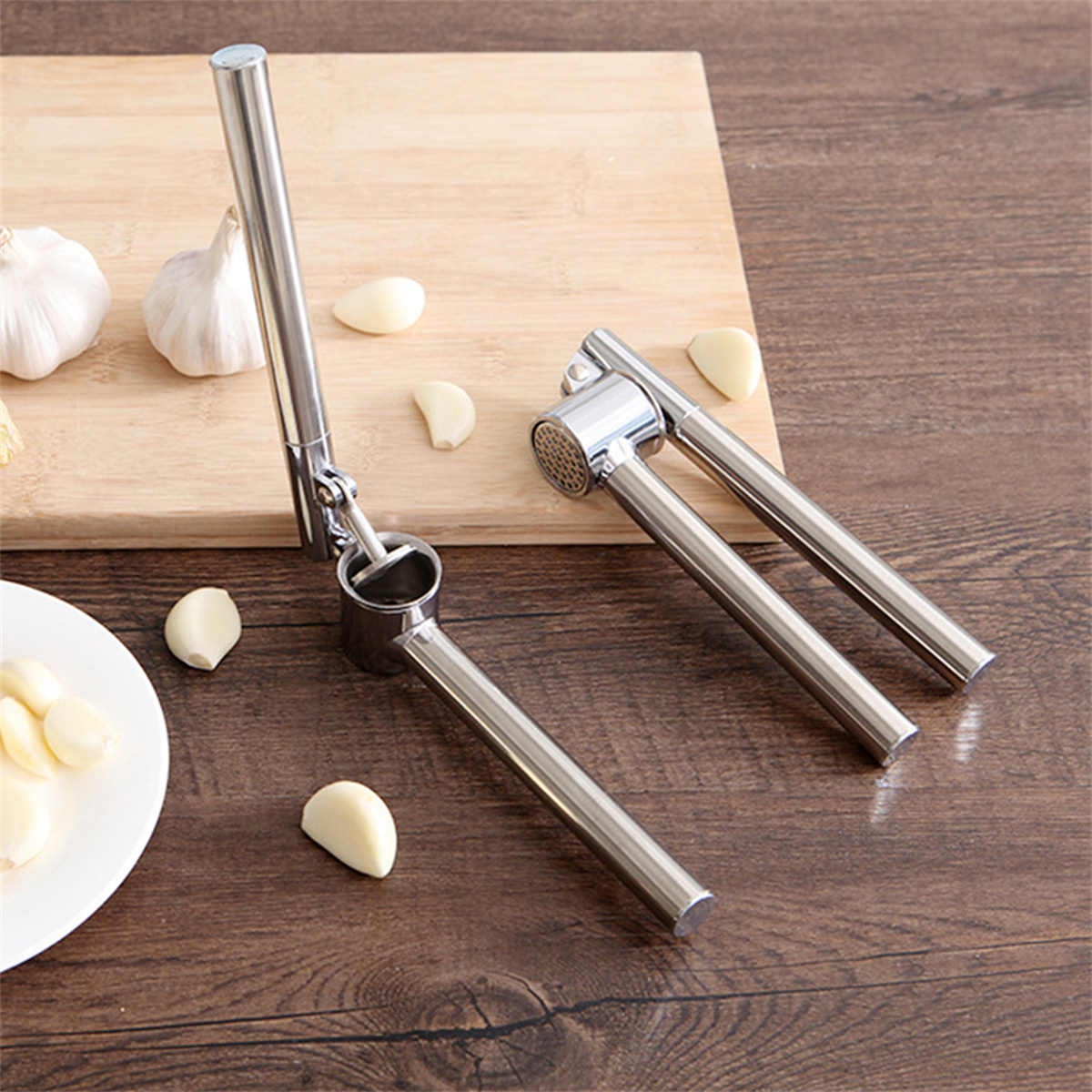 Knoblauchpresse mit Knoblauchzehen auf einem Holzbrett, daneben ganzer Knoblauch.