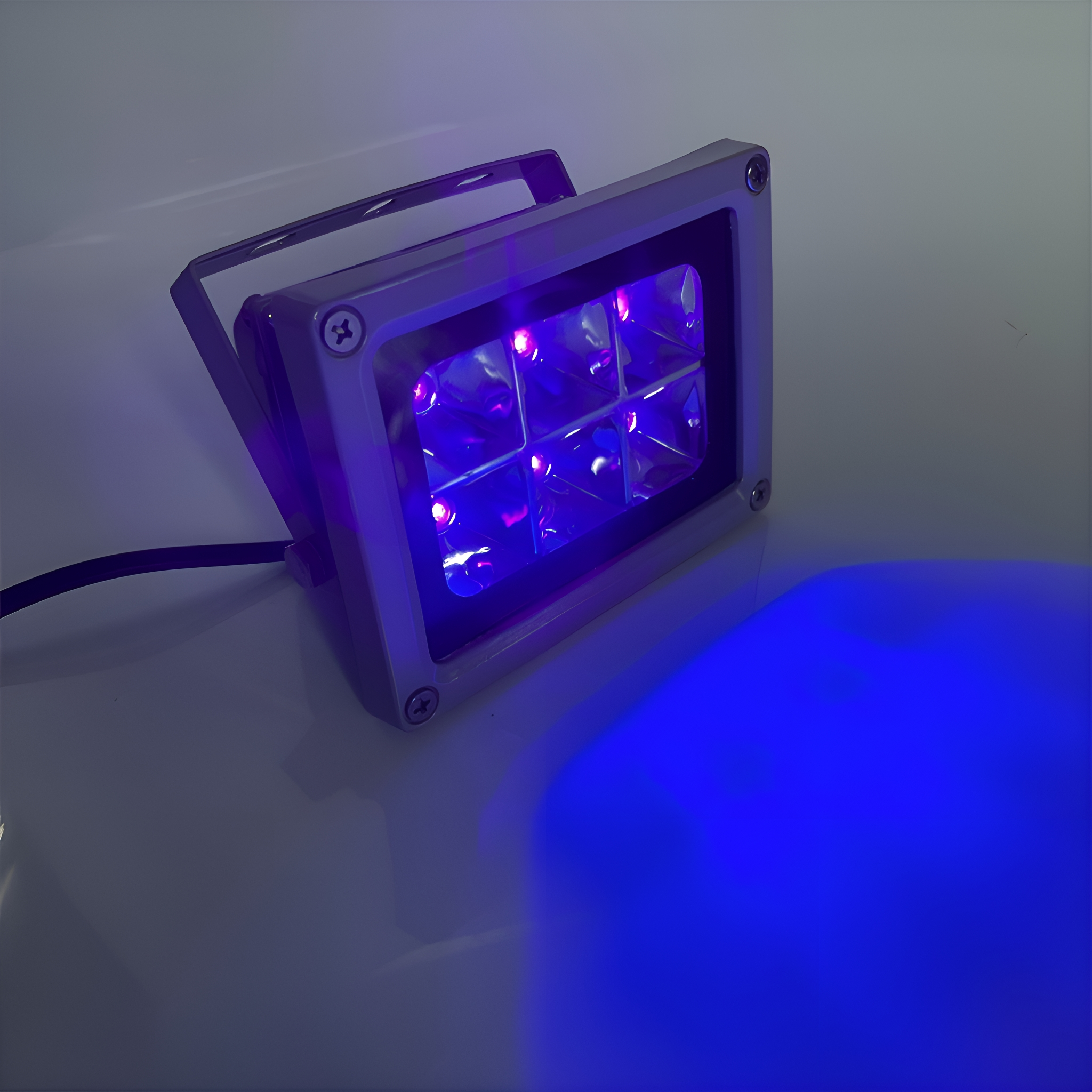 UV-Licht mit sechs beleuchteten Quadraten, wirft einen blauen Schein auf weiße Fläche.
