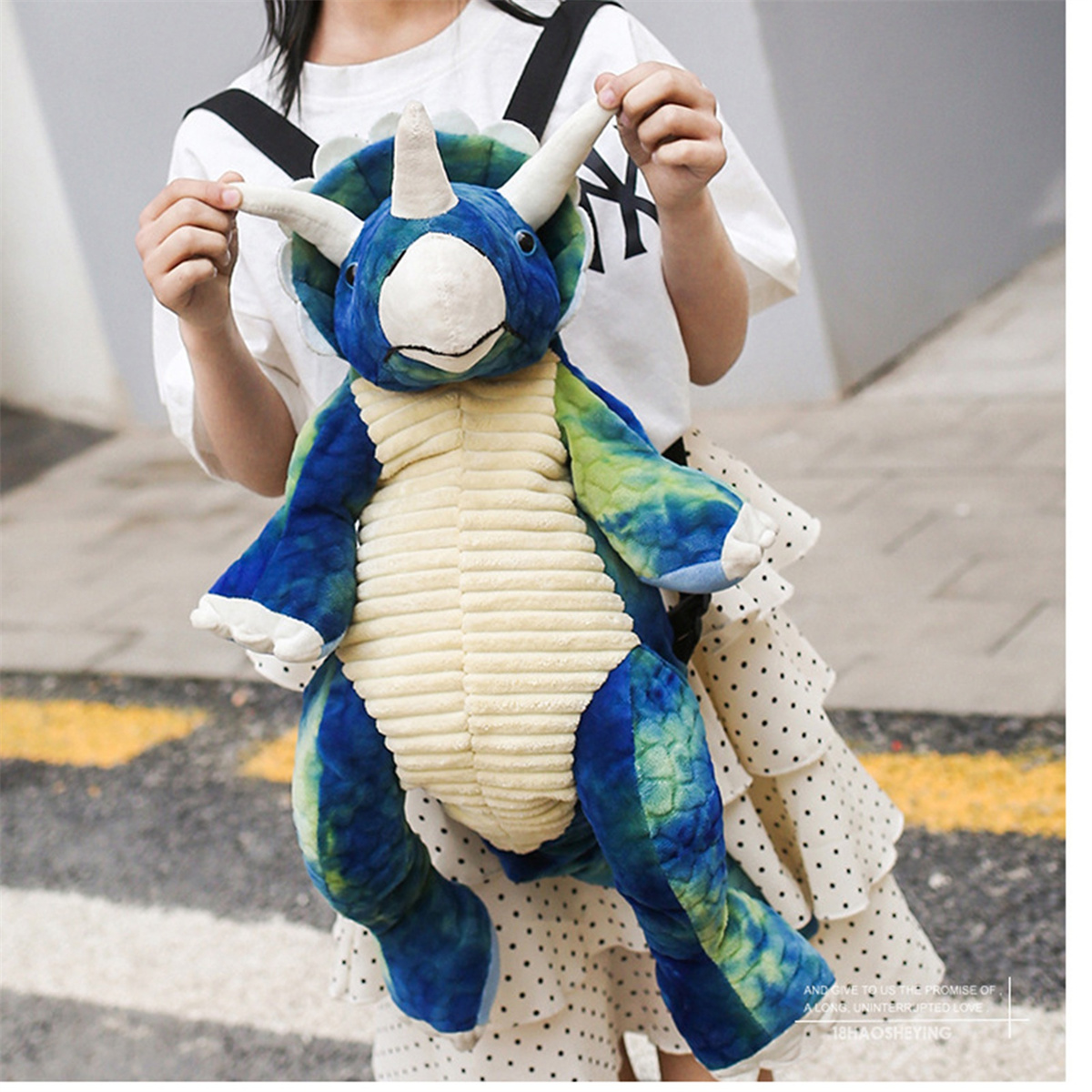 Ein Plüsch-Triceratops-Spielzeug in Blau und Grün, gehalten von einer Person mit weißem Hemd.