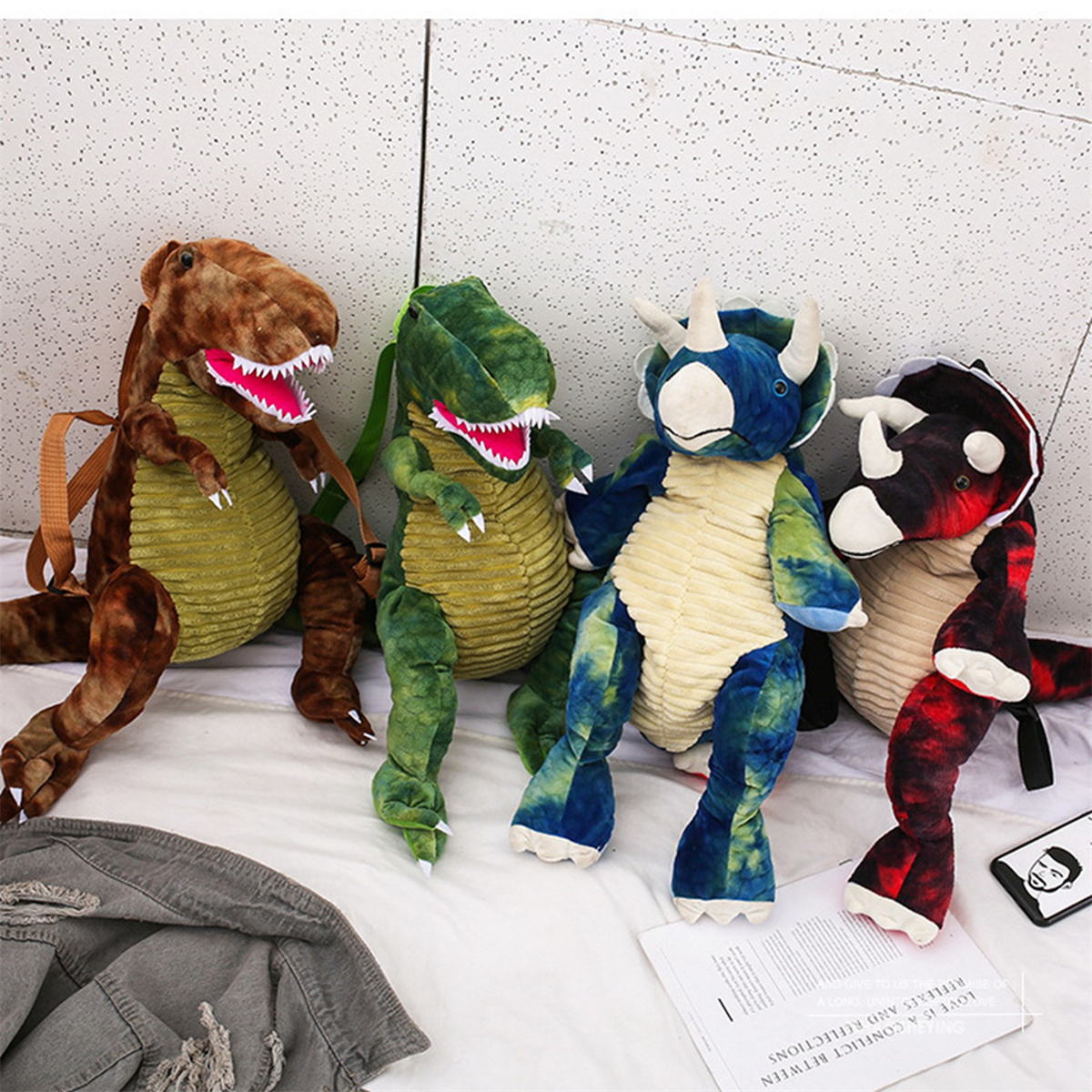Vier Stoff-Dinosaurier-Rucksäcke. Verschiedene Farben und Designs von Dinosaurier-Plüschtieren.