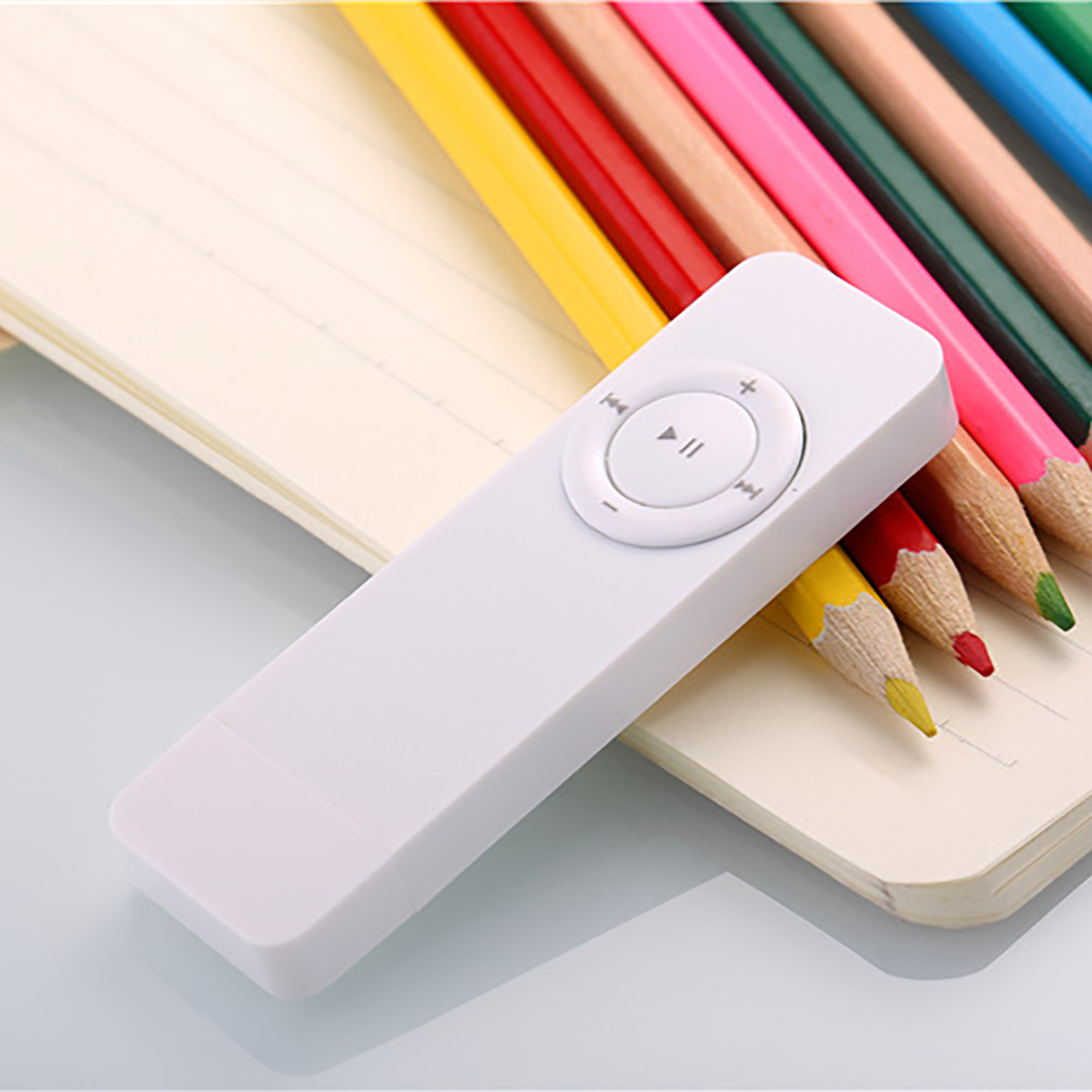 Weiße Fernbedienung mit Play/Pause-Taste auf einem Notizbuch mit Buntstiften.