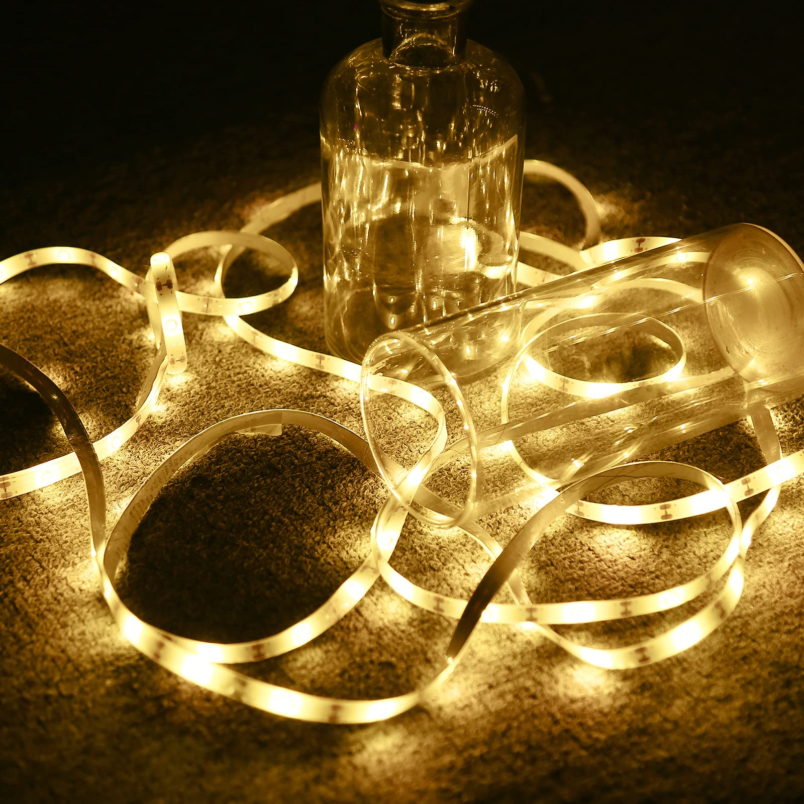 Eine Glasflasche und ein Glas mit einer Lichterkette. Die Lichter sind gelb und auf einem Teppich.