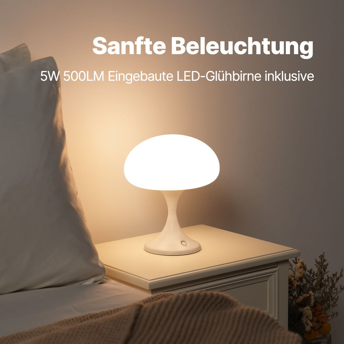 Eine weiße pilzförmige Lampe auf einem Nachttisch. Sie steht neben einem Kissen und einer Decke. Sanftes Licht.