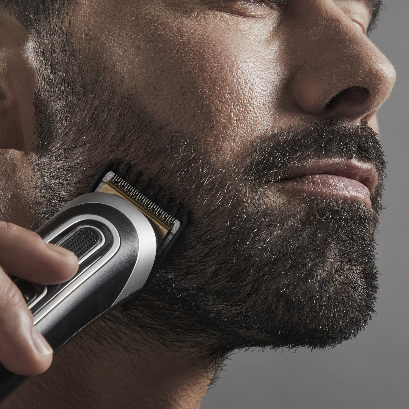 Un hombre se afeita la barba con un recortador negro y plateado, toma cercana.