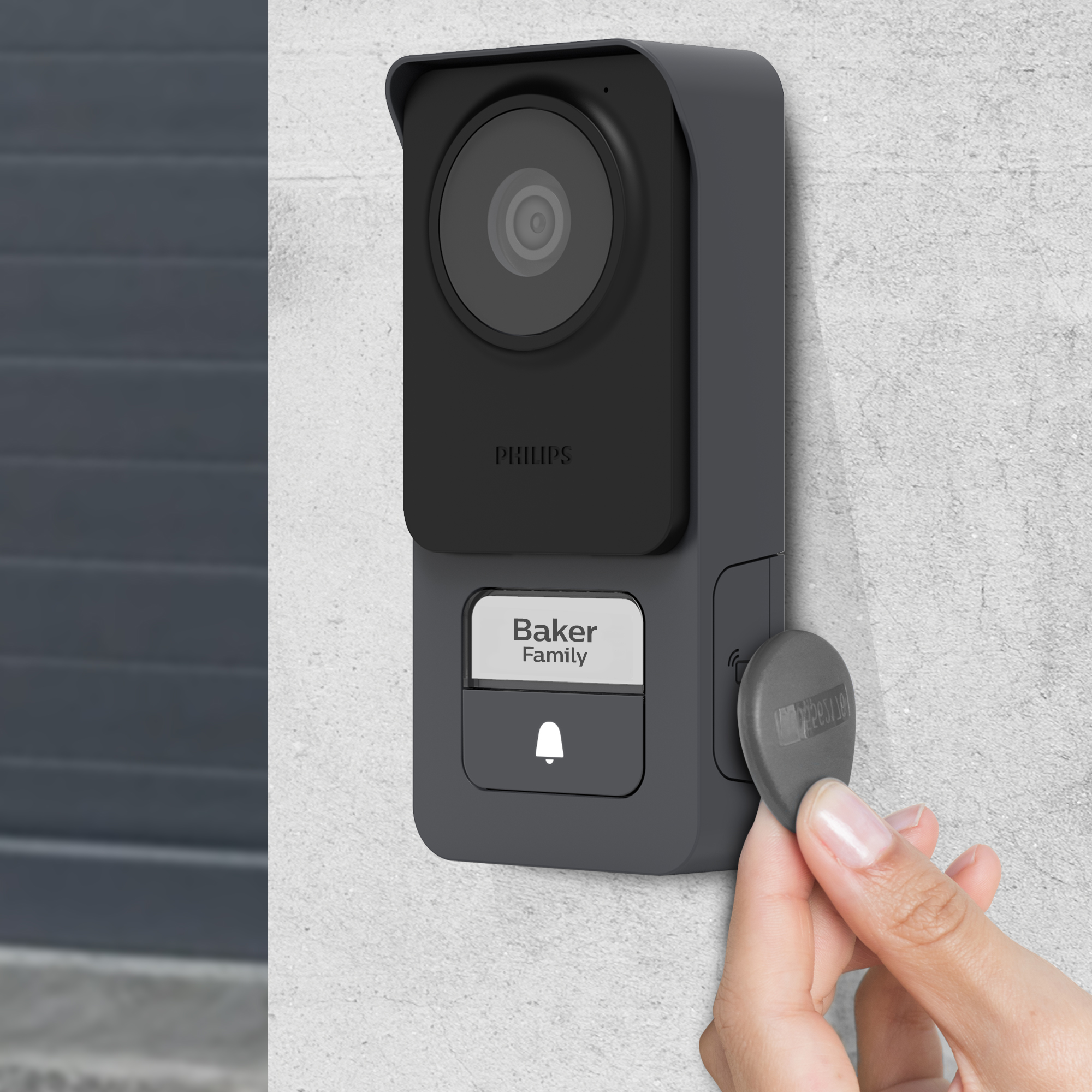 Un timbre Philips negro con cámara, una placa con el nombre Familia Baker y una mano sosteniendo una llave gris.