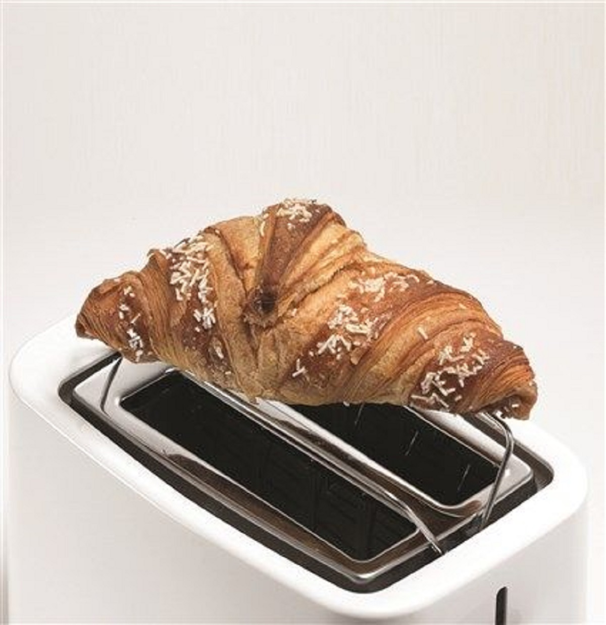 Un croissant è su un tostapane bianco. È marrone e ha delle decorazioni bianche.