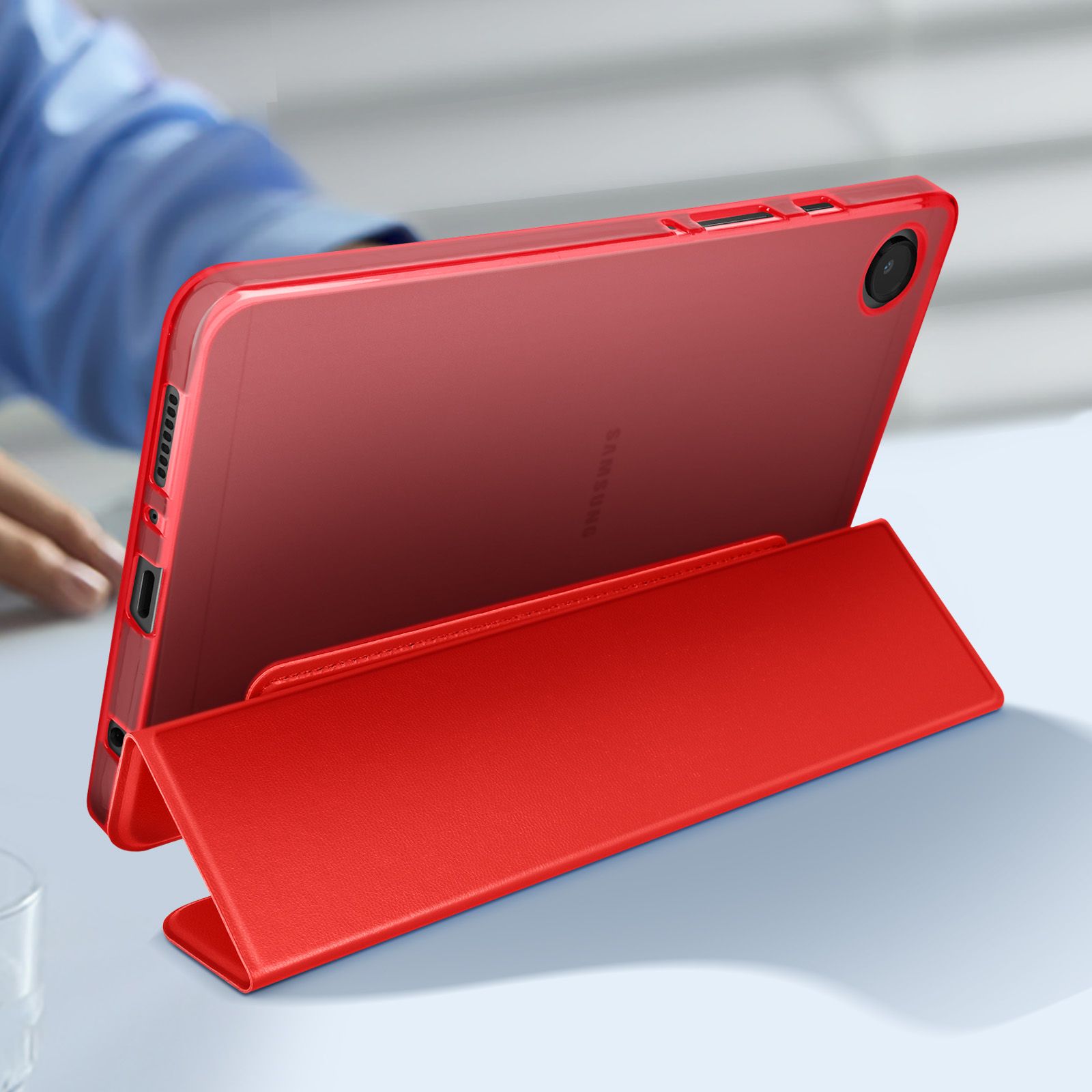 Tablet rosso con custodia rossa, la custodia è aperta. Un tavolo sotto e mani visibili.