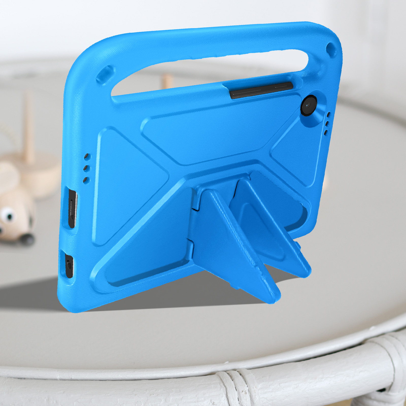 Blaue Tablethülle mit Ständer und Griff auf weißem Tisch. Spielzeug und Hintergrund sichtbar.