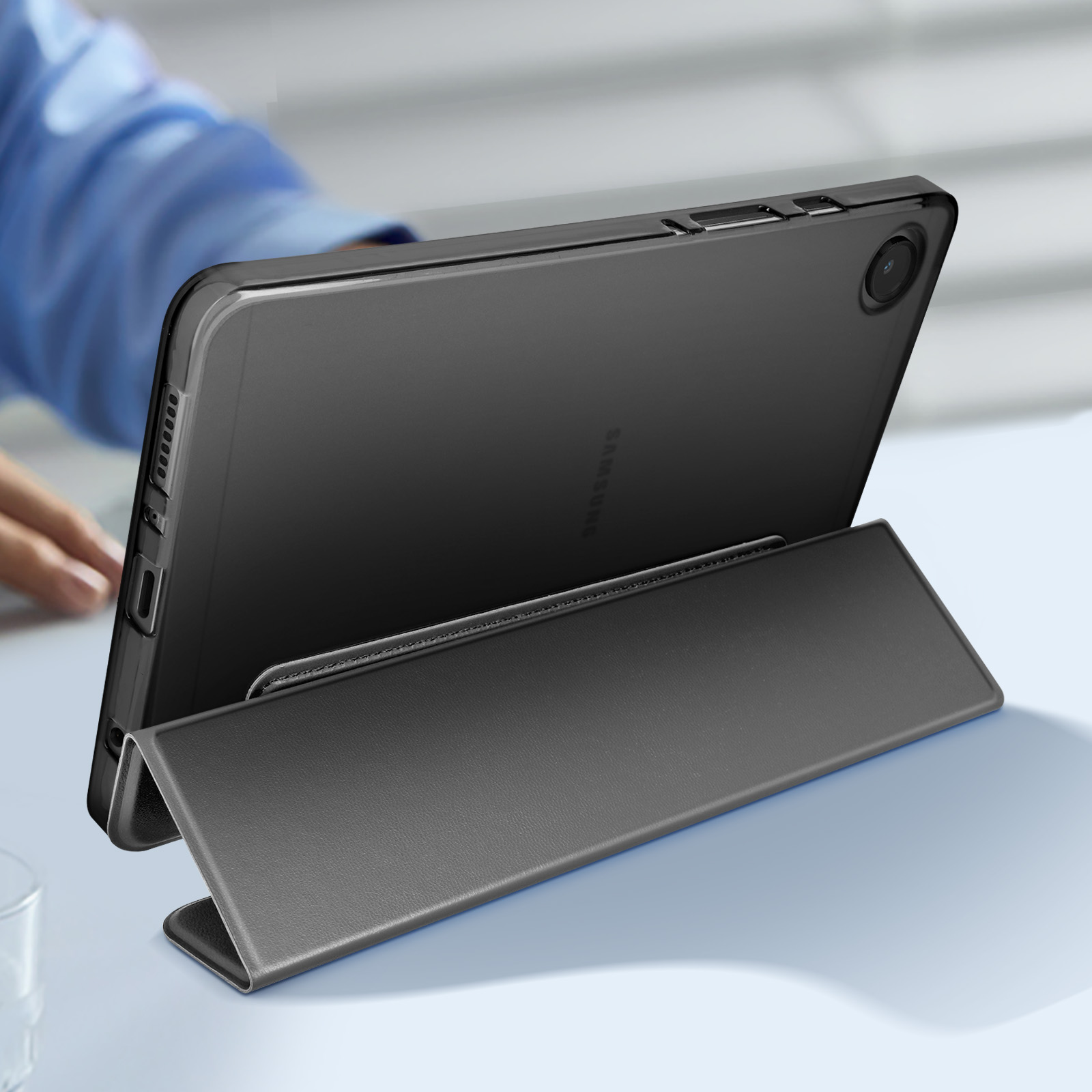 Custodia nera per tablet con supporto. Sono visibili la mano di una persona e un tavolo blu.