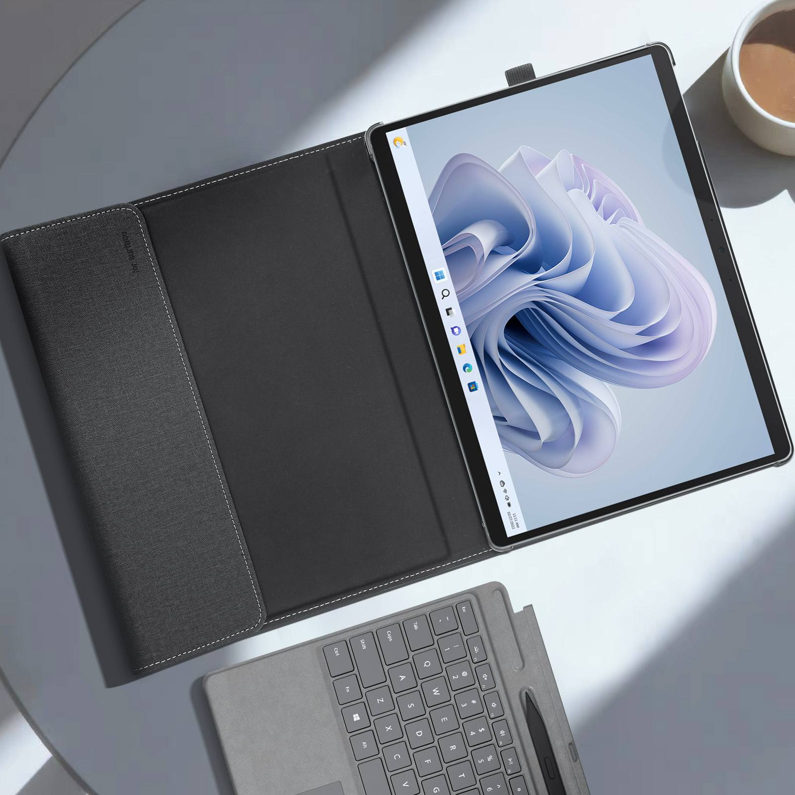 Tablet con custodia aperta, tastiera e tazza di caffè su una superficie bianca.