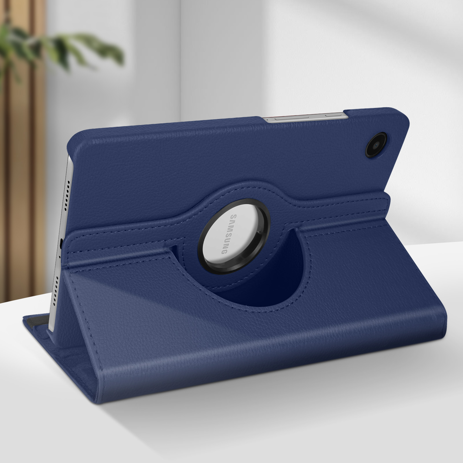 Custodia blu per tablet con anello girevole, appoggiata su una superficie. Sfondo sfocato.
