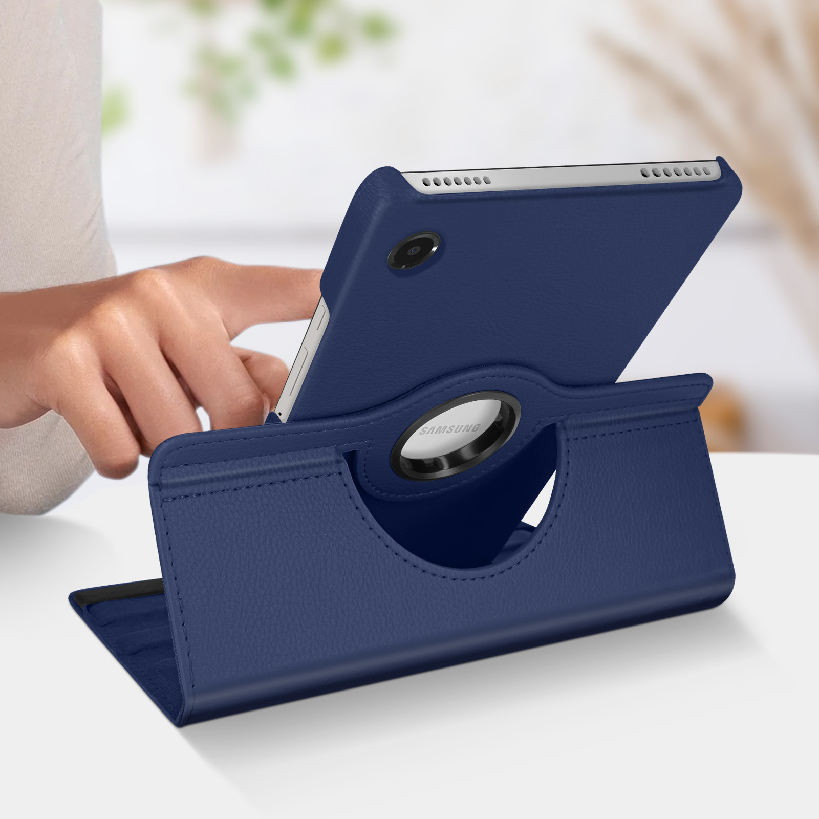 Custodia blu per tablet con supporto, mano sul tavolo. Il tablet ha una cornice argentata.