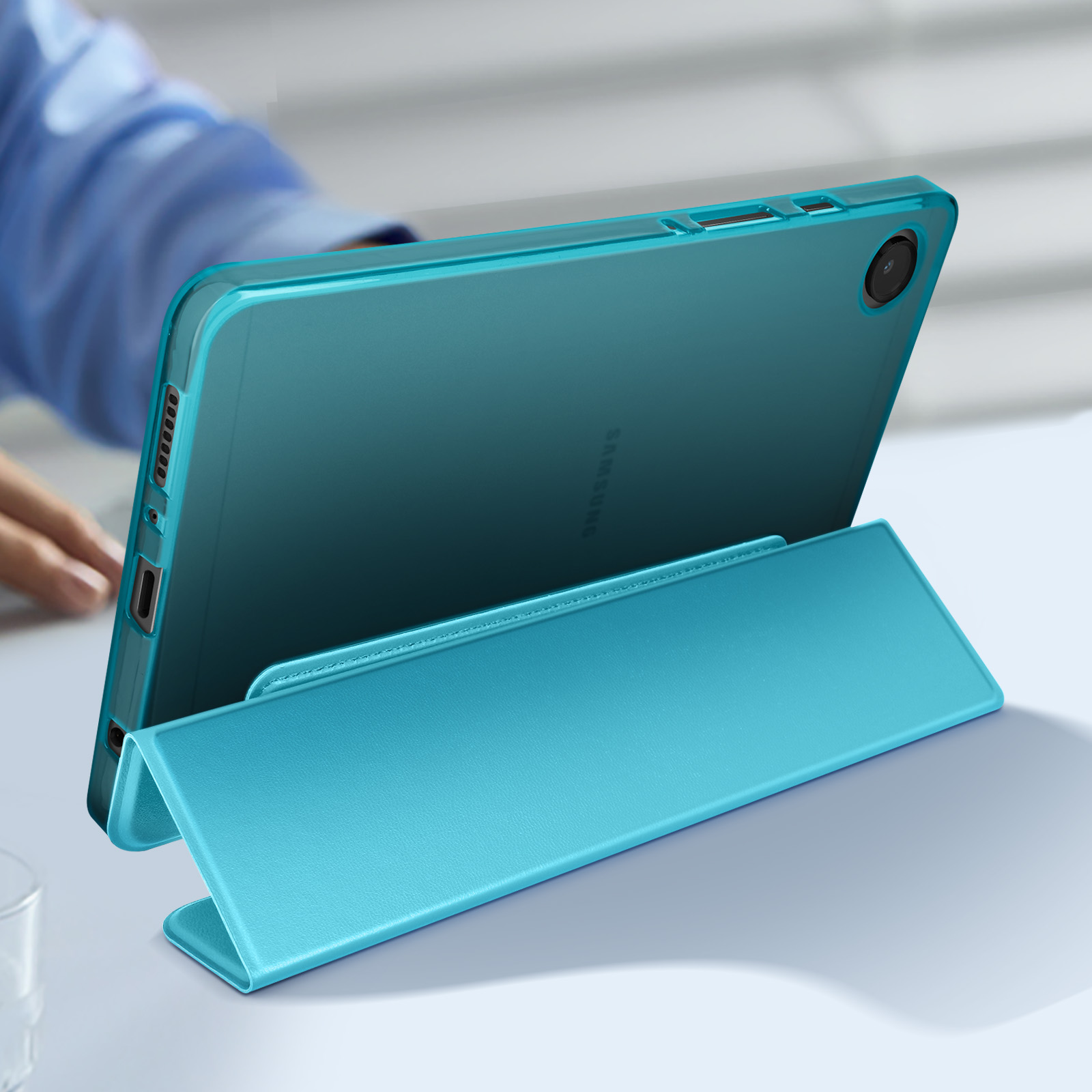 Tablet turchese in una custodia, sostenuto da un supporto. Sfondo chiaro.