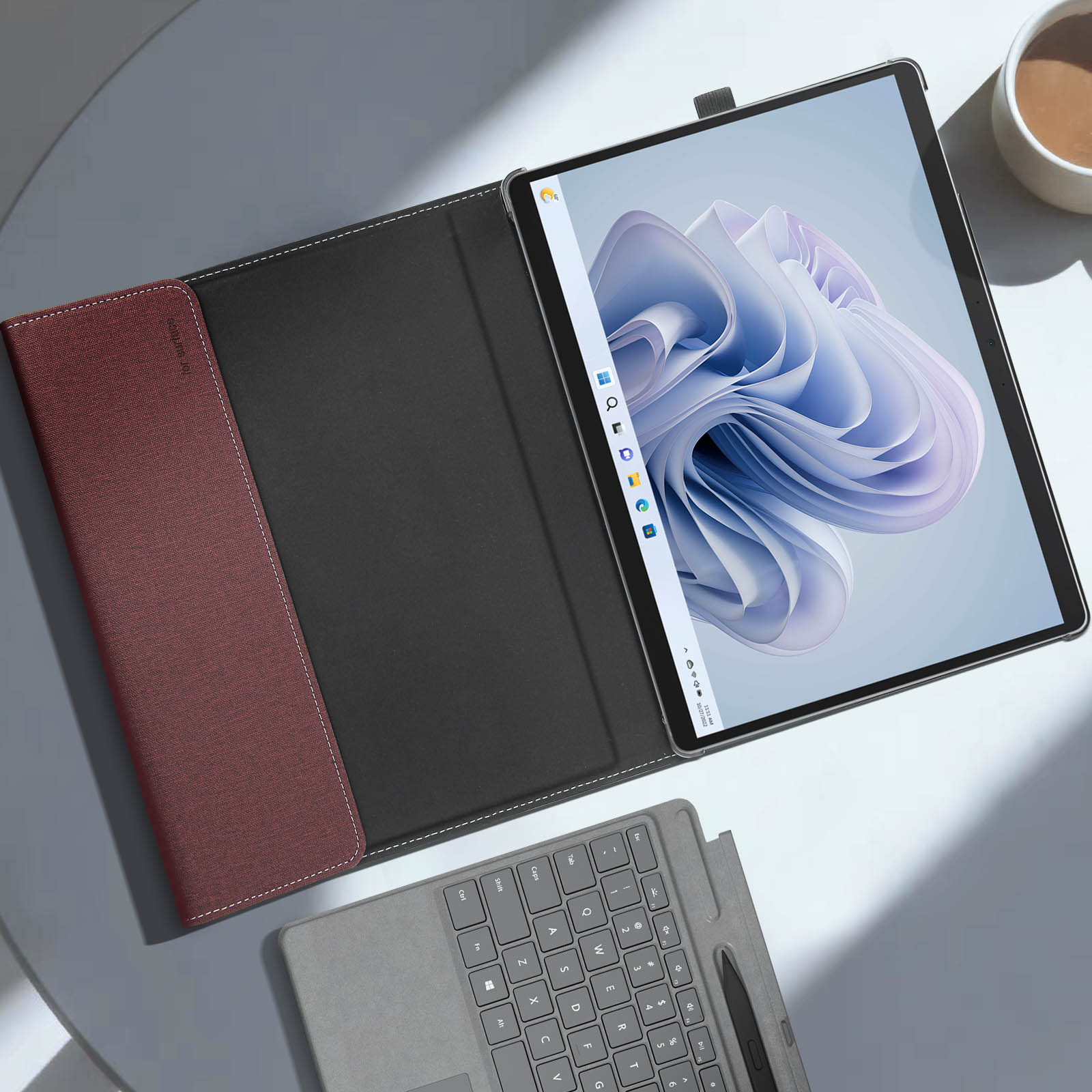 Tablet in una custodia con tastiera sul tavolo. Tazza di caffè e tastiera visibili. Superficie bianca.