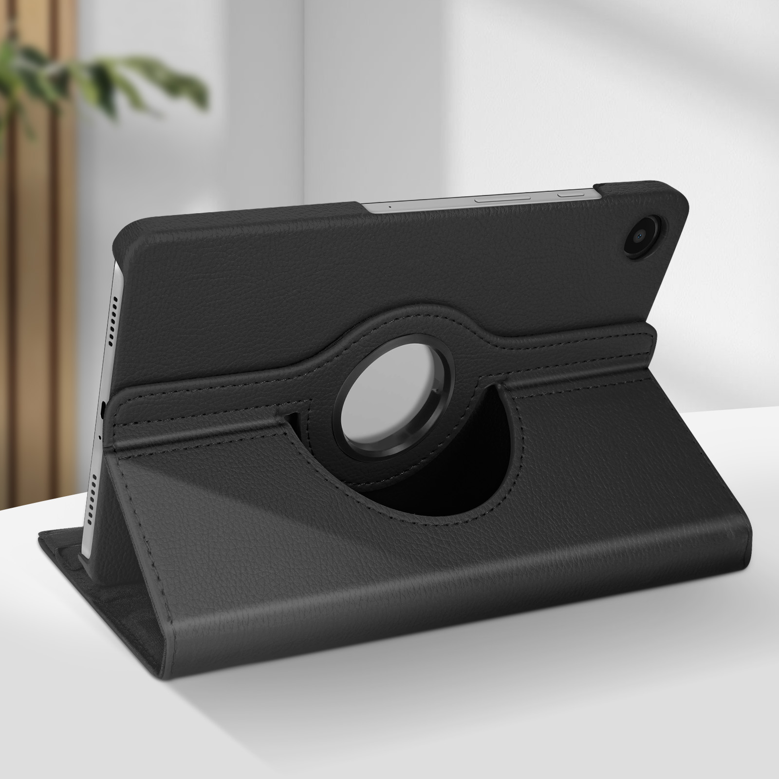 Tablet nero in una custodia nera, sollevato. Sfondo: un muro bianco sfocato e un po' di verde.