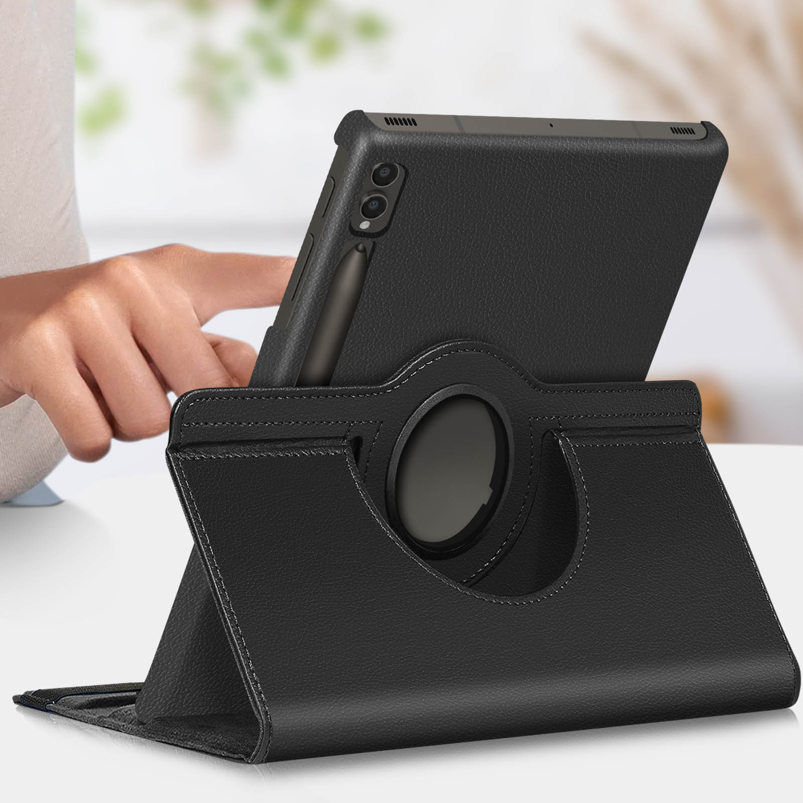 Tablet in una custodia nera, su un supporto. Una mano sta usando il tablet. Tazza bianca sullo sfondo.