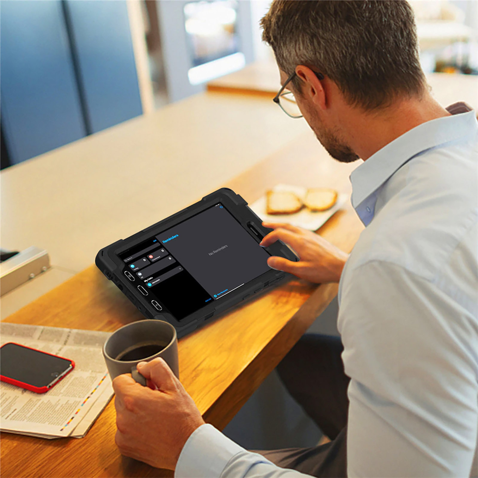 Mann benutzt Tablet mit Hülle, auf einem Holztisch. Kaffee und Telefon im Hintergrund.