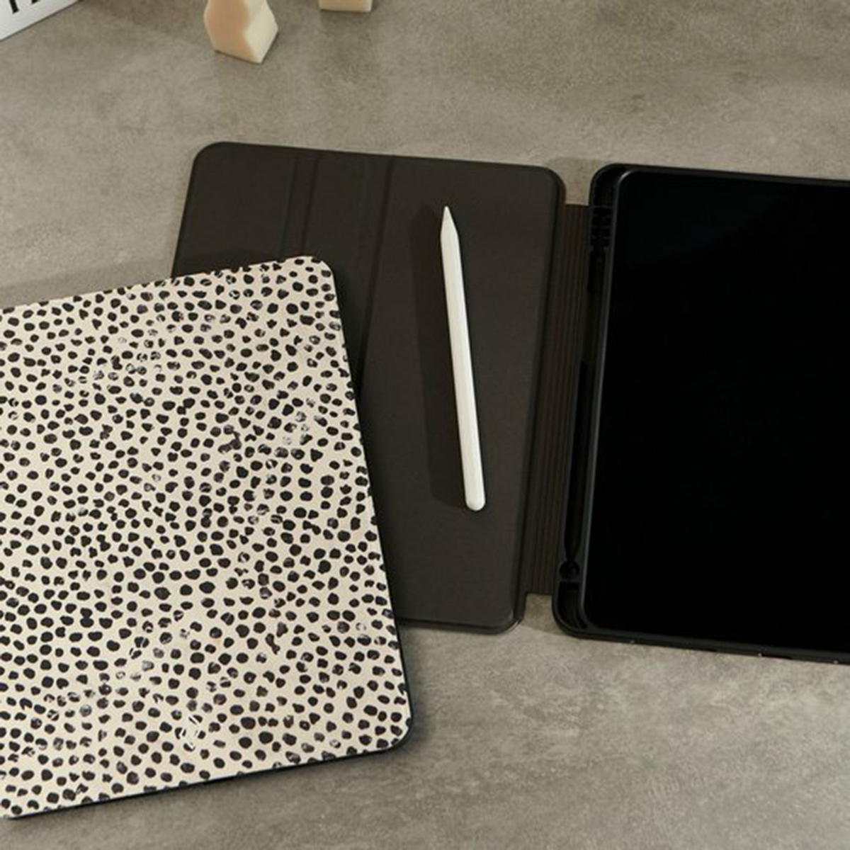 Tablet met zwart scherm, een pen en een hoesje met een stippenontwerp op een oppervlak.