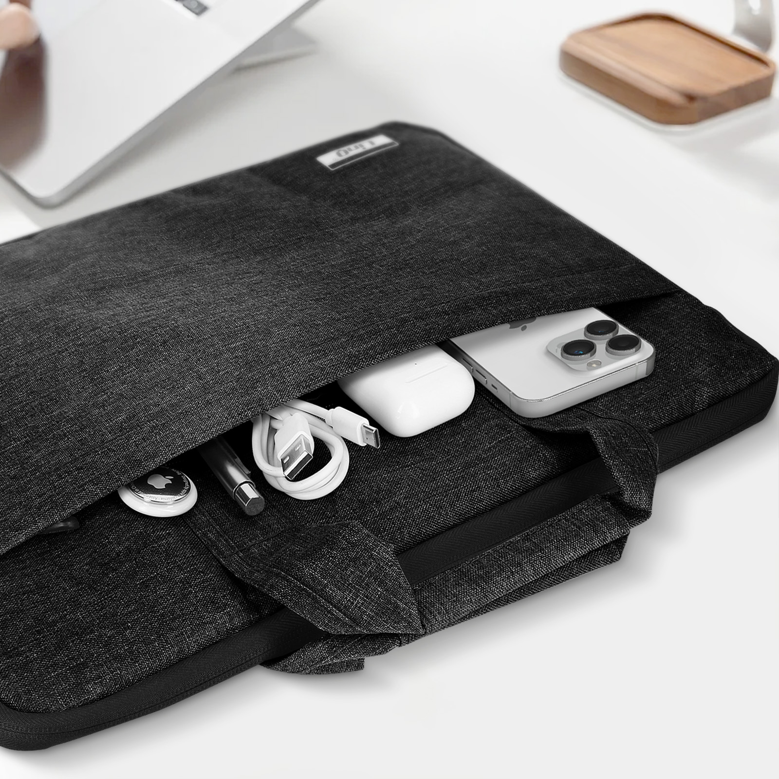 Funda para portátil negra con objetos dentro. Fondo blanco.