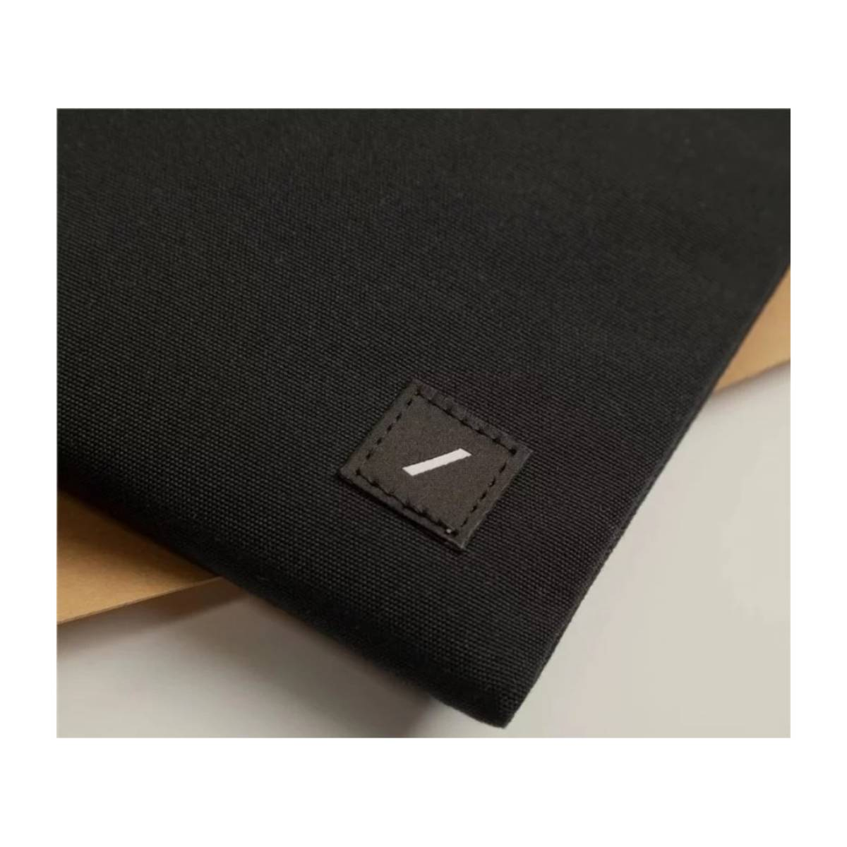 Un étui noir et rectangulaire avec un petit logo carré sur le devant. Le logo est blanc.