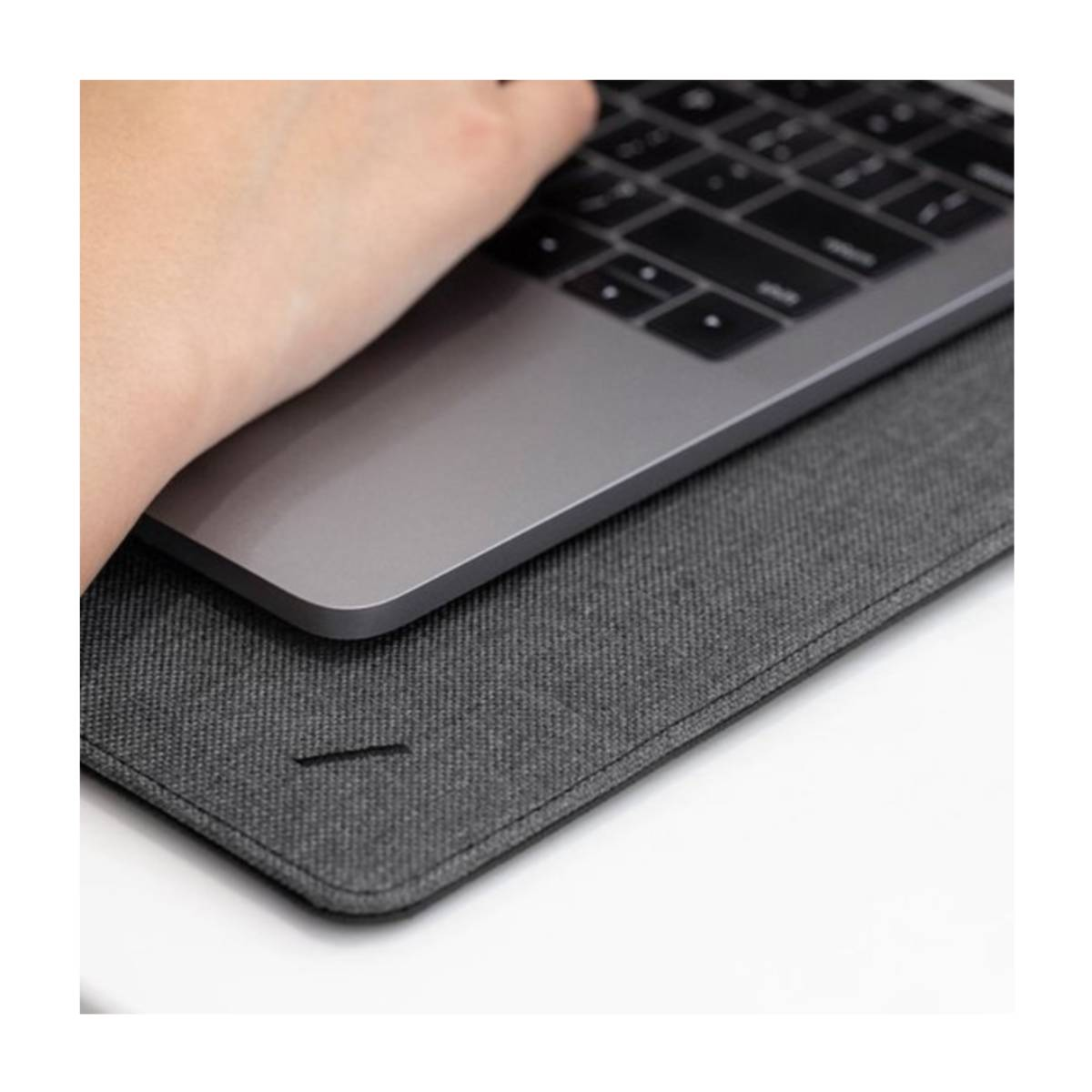 Mano tocca un laptop. Laptop su una cover grigia. Superficie bianca. Cover grigia ha una cucitura.