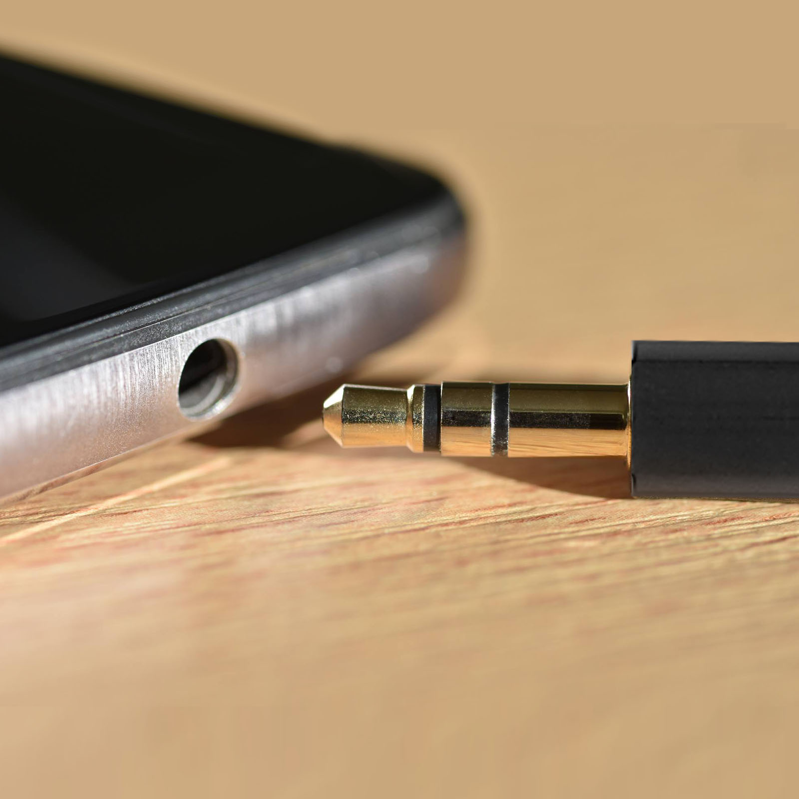 Primo piano di un jack da 3,5 mm collegato a un telefono. Sfondo con superficie in legno.