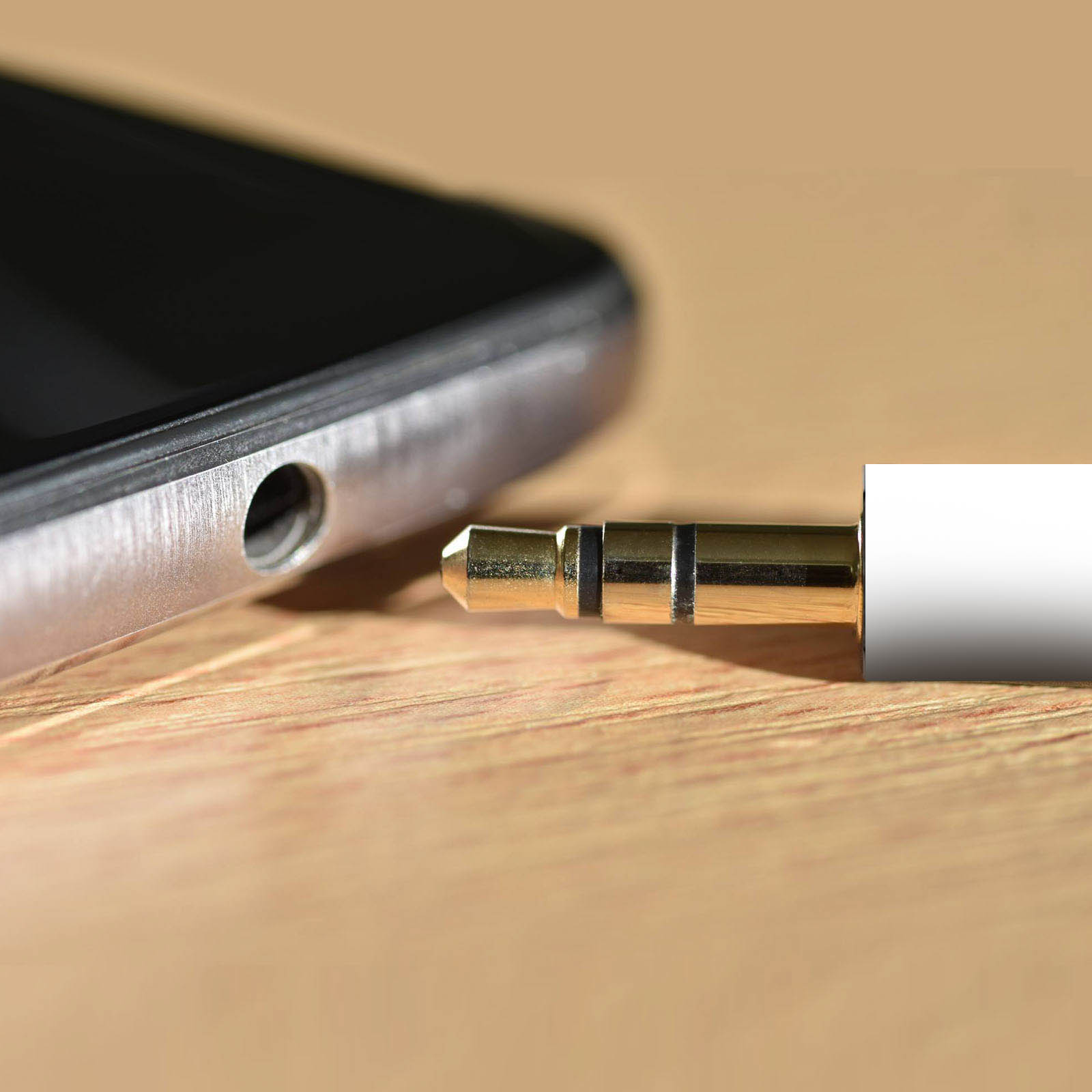 Jack audio da 3,5 mm collegato a uno smartphone, su una superficie di legno.