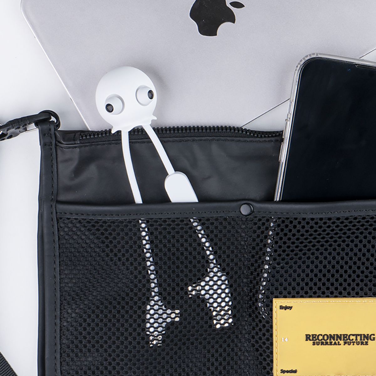 Borsa nera con laptop, telefono e oggetto a forma di teschio.