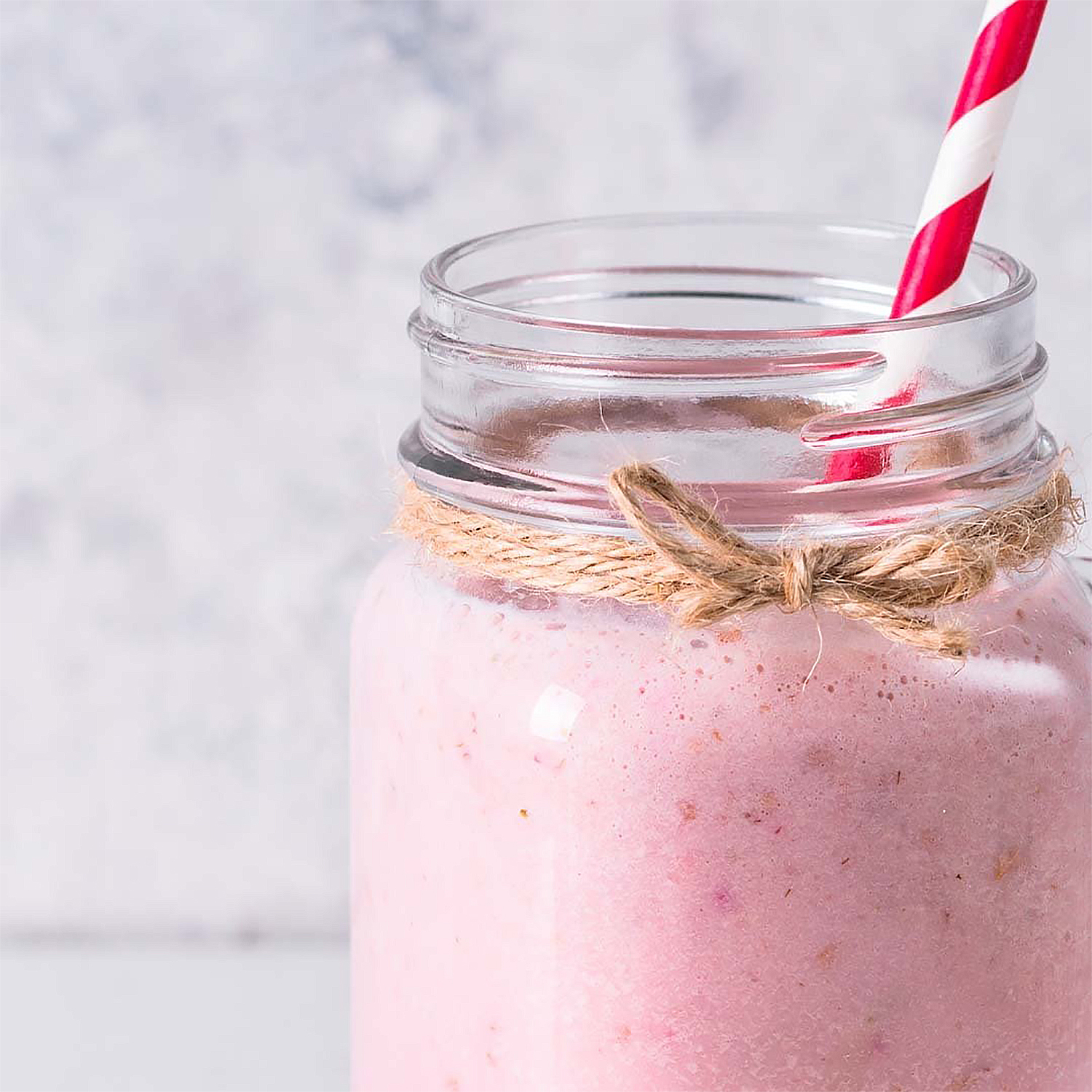 Un frullato rosa in un barattolo con cannuccia e spago.