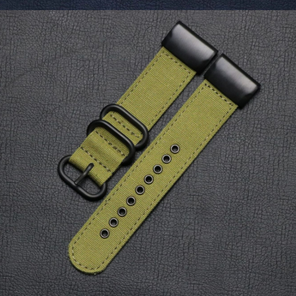 Zwei olivgrüne Uhrenarmbänder mit schwarzer Hardware. Auf einem strukturierten dunklen Hintergrund liegend.