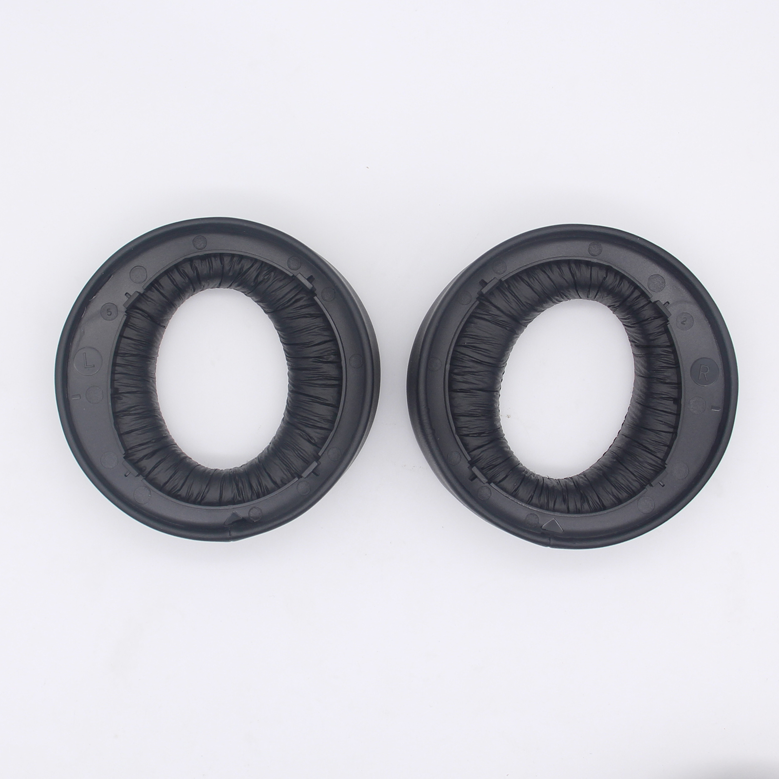Due cuscinetti auricolari ovali neri con un design circolare e scanalato su sfondo bianco.