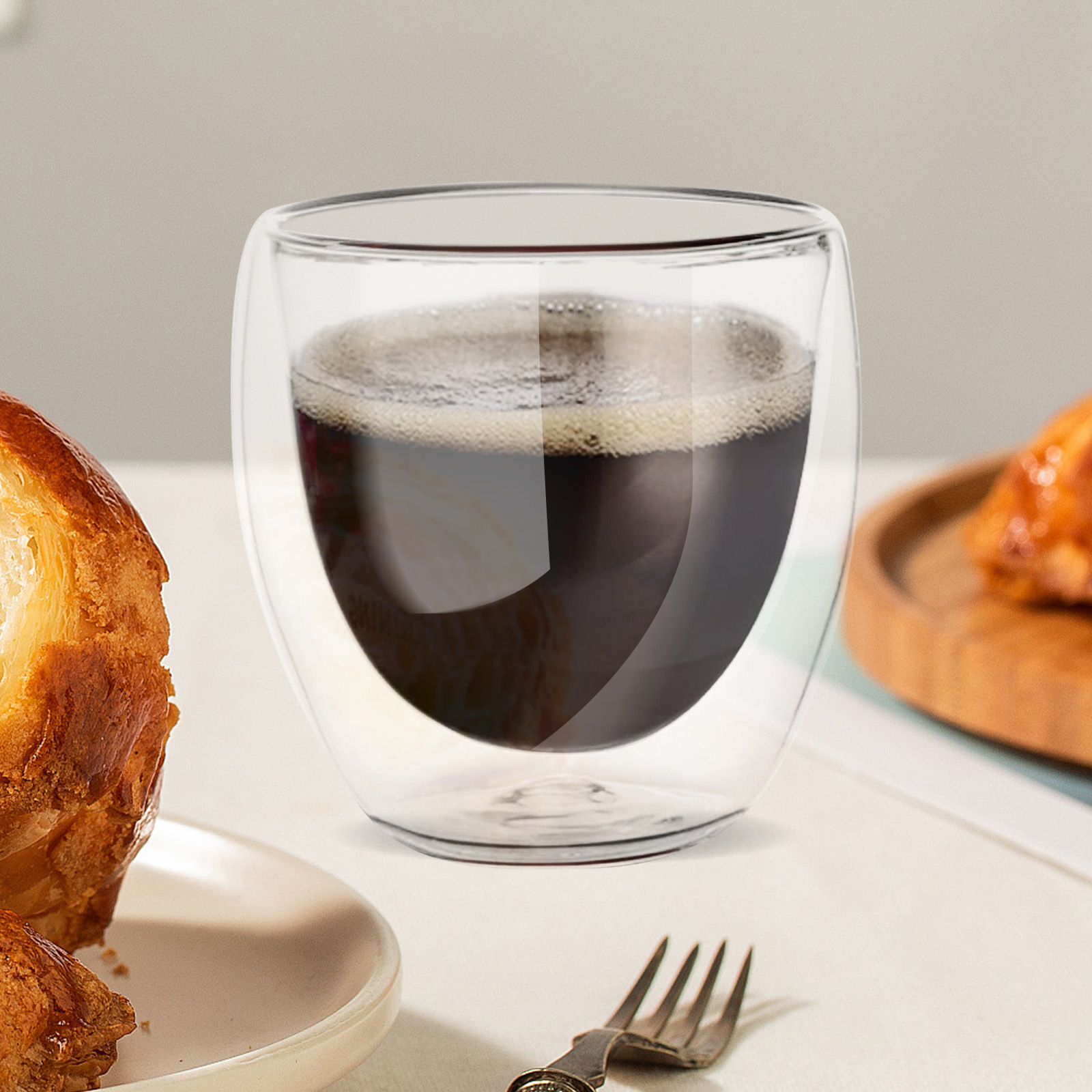 Doppelwandiges Glas mit Kaffee, Gebäck und Gabel auf einem Tisch.
