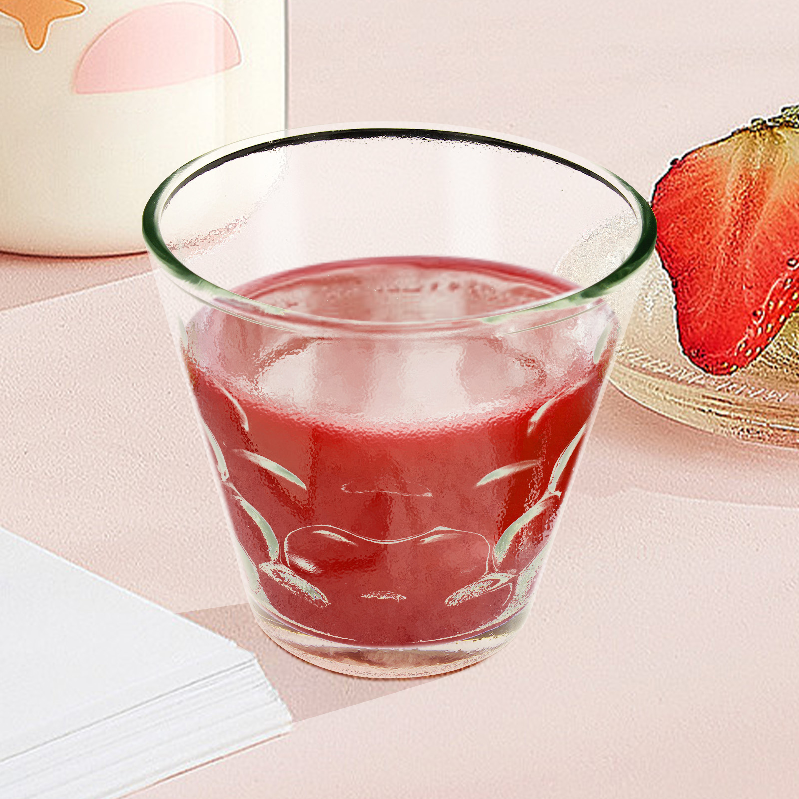 Ein Glas mit rosa Saft und einer Erdbeere auf einer rosa Oberfläche.