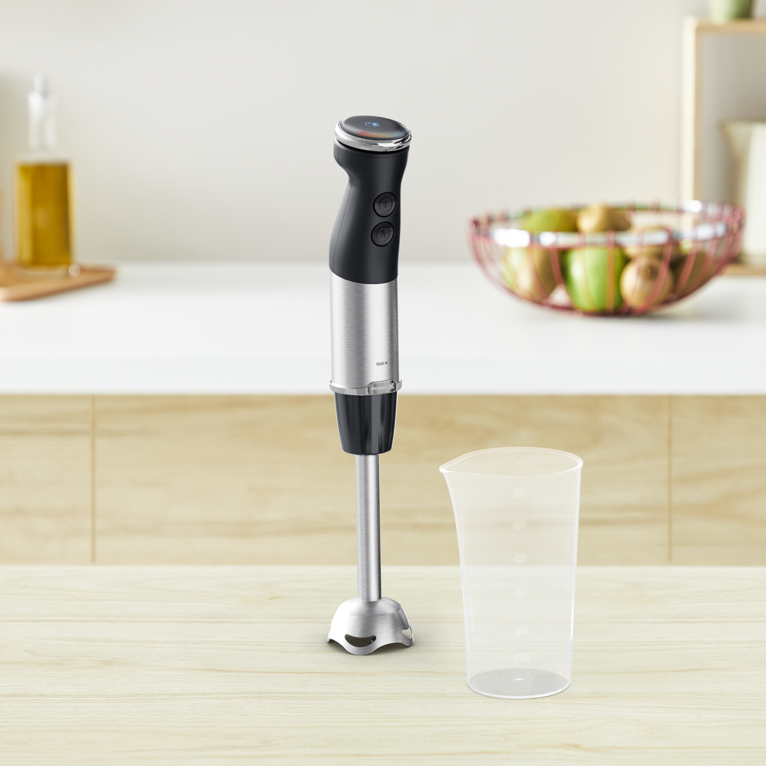 Blender ręczny z pojemnikiem i miską owoców na drewnianej powierzchni.