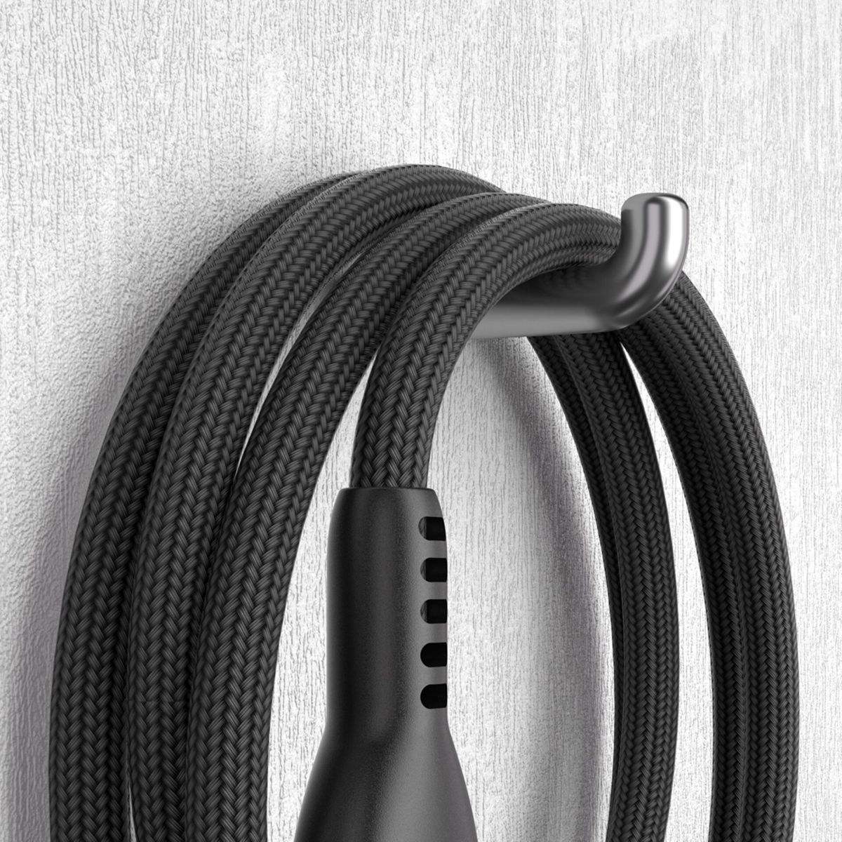 Ein schwarzes geflochtenes Ladekabel hängt an einem silbernen Haken an einer weißen Wand. Das Kabel ist aufgerollt.