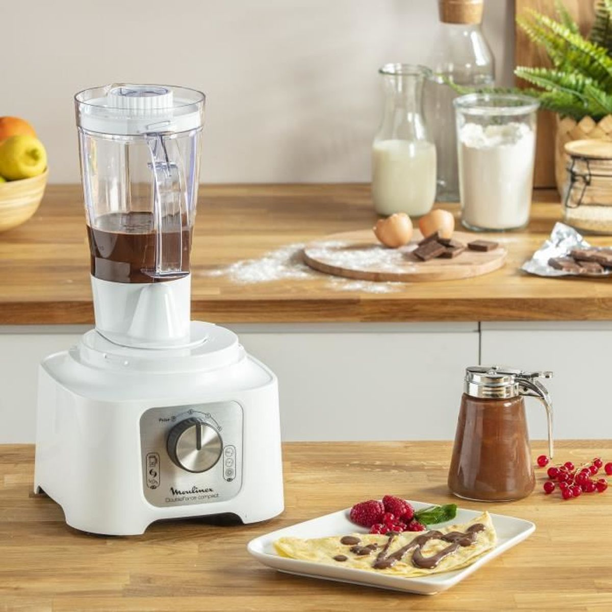 Un robot da cucina bianco con un contenitore trasparente e cibo all'interno, su una superficie in legno.