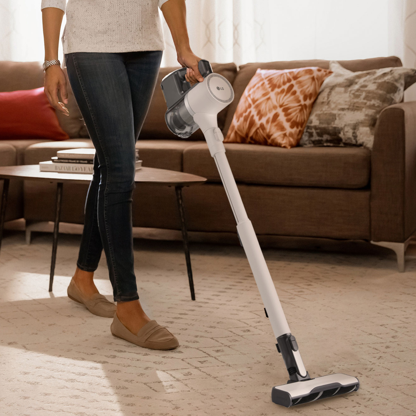 Donna che usa un aspirapolvere senza fili LG bianco e grigio su un tappeto.