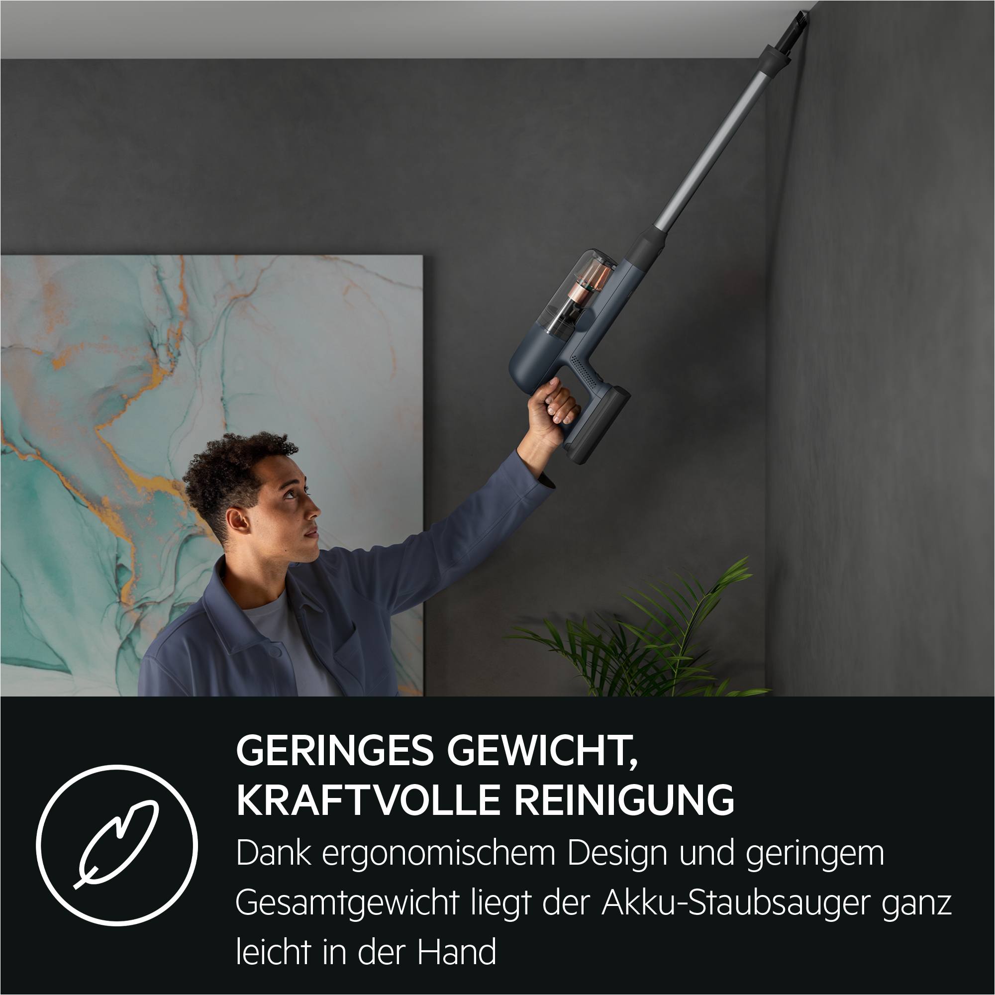 Ein Mann staubsaugt eine Wand mit einem blauen und grauen kabellosen Staubsauger.