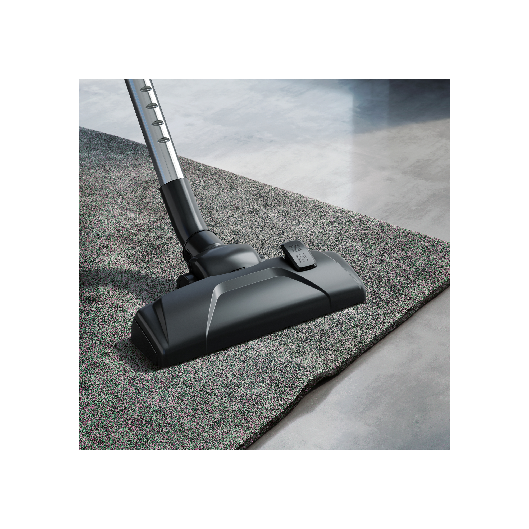 Głowica odkurzacza na szarej wykładzinie, odkurzacz jest czarny i srebrny.