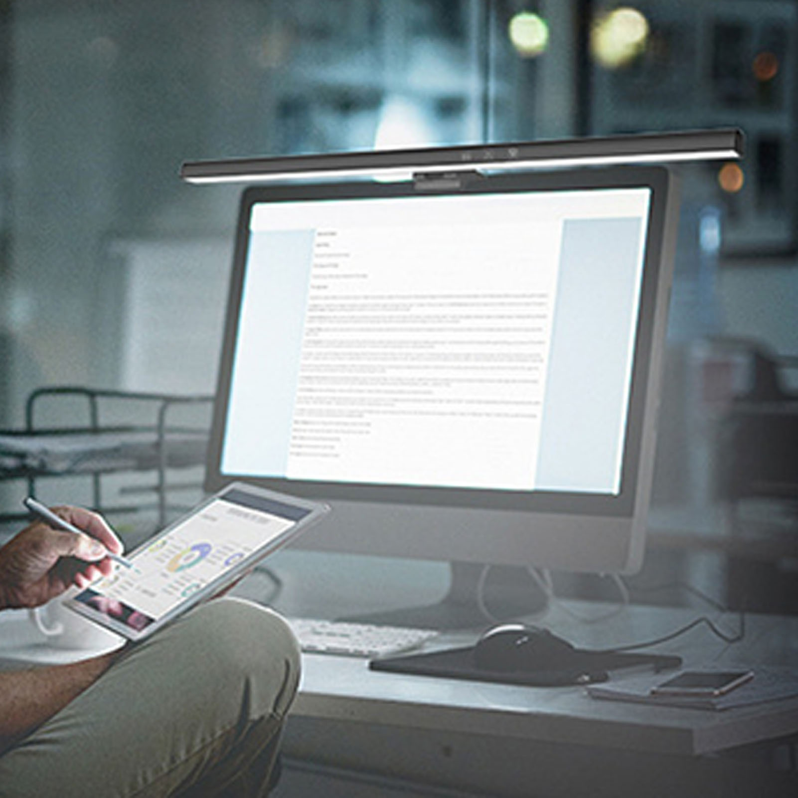 Person, die ein Tablet und einen Stift in der Nähe eines Computermonitors mit einer Schreibtischlampe verwendet.