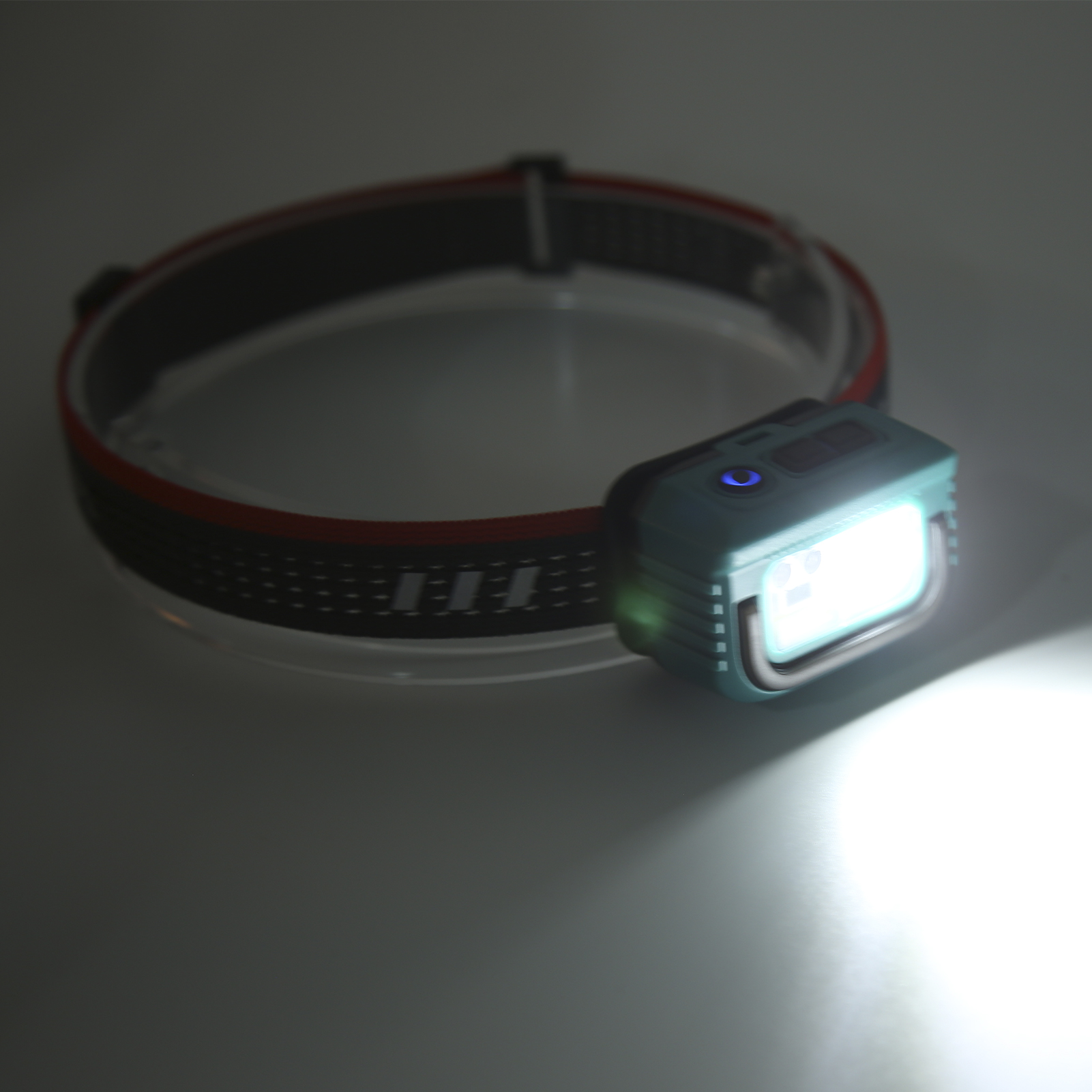 Stirnlampe an einem schwarz-roten Riemen, die einen hellen Strahl aussendet. Die Bedienelemente sind sichtbar.