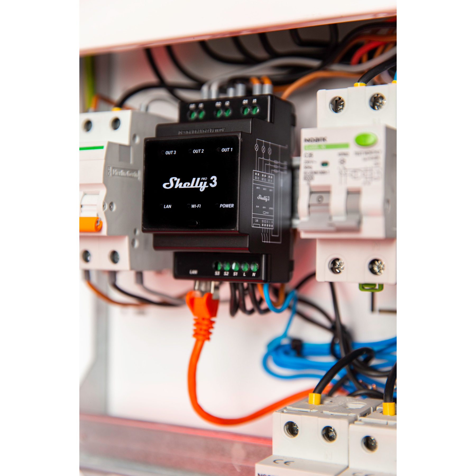 Czarne urządzenie smart home Shelly 3 zainstalowane w panelu elektrycznym. Pomarańczowe i czarne przewody są podłączone.