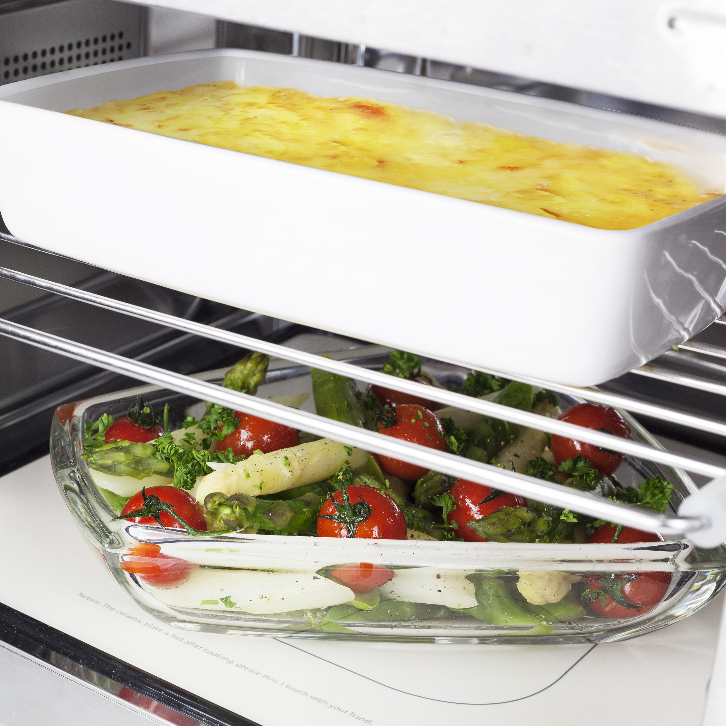 Un forno con due piatti di vetro all'interno, uno con lasagne e l'altro con verdure.